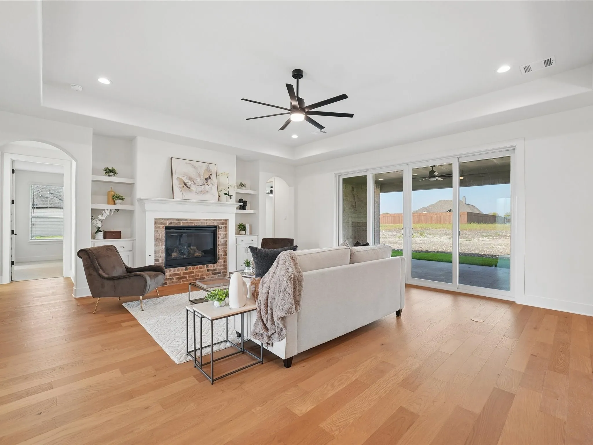 Living area with wood-finish flooring, a brick fireplace with a white mantel, and built-in shelving