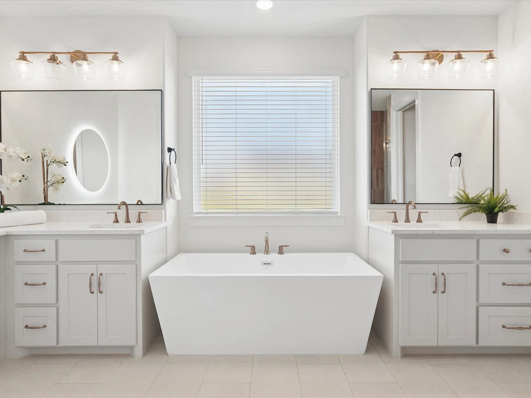 Freestanding soaking tub centered under a window with blinds, flanked by dual vanities