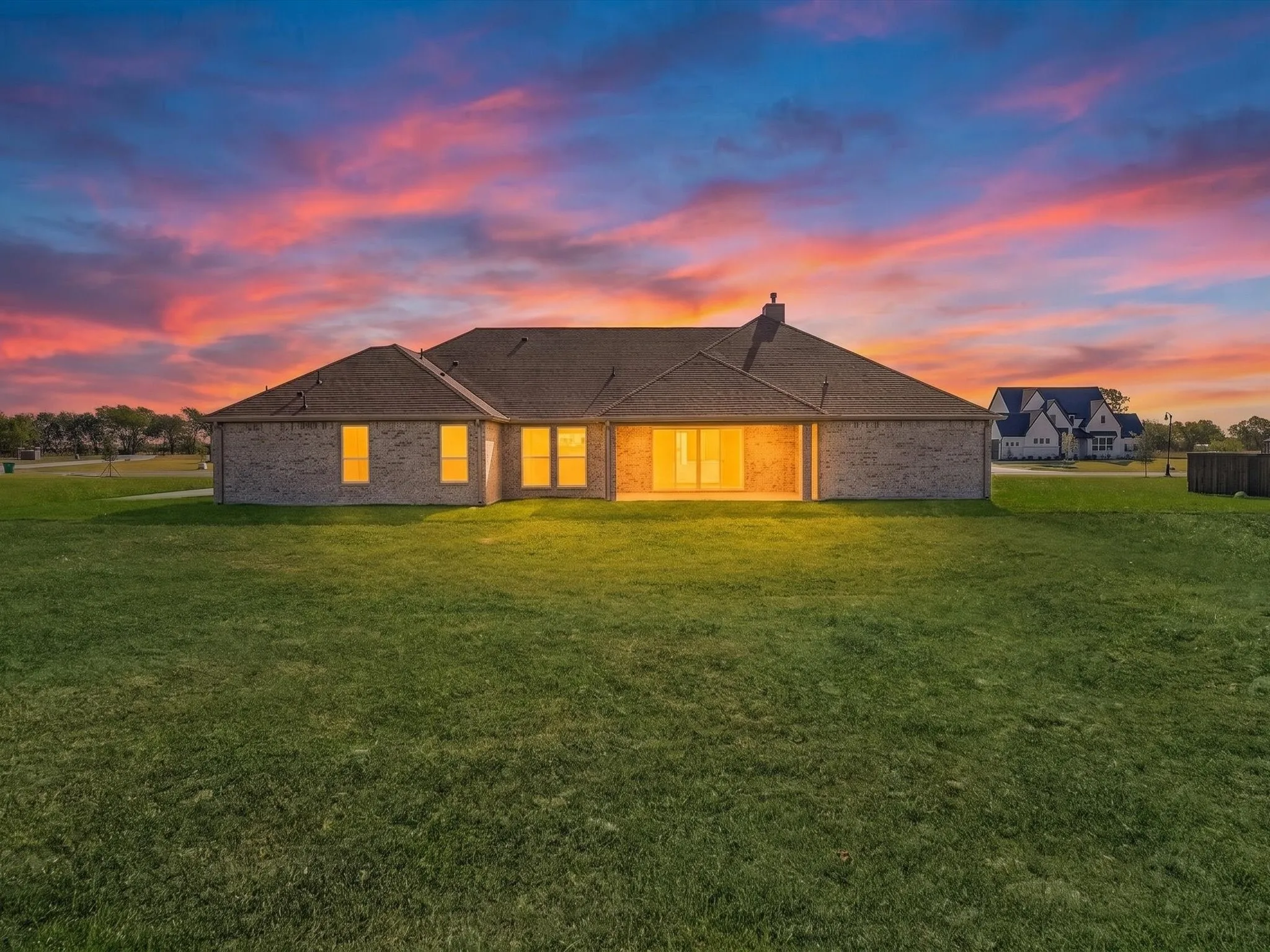 Expansive green lawn, brick exterior, multiple windows, covered patio, and a shingle roof