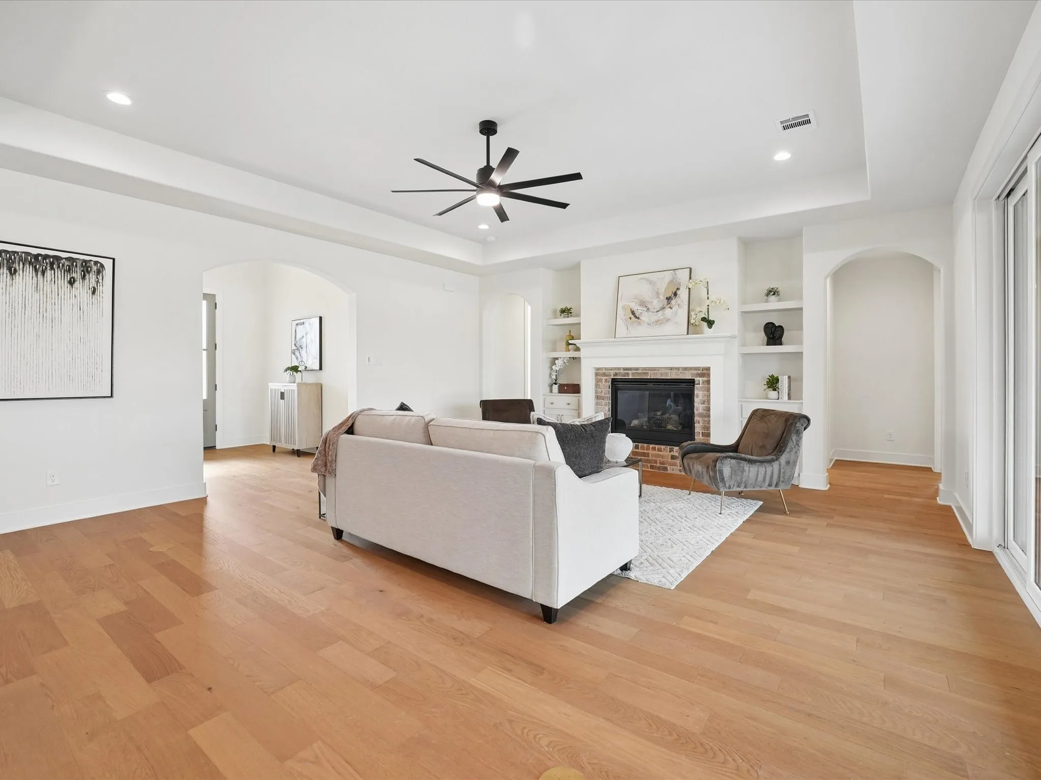 Wood-finish flooring, recessed lighting, tray ceiling, brick fireplace with mantel, and built-in shelving