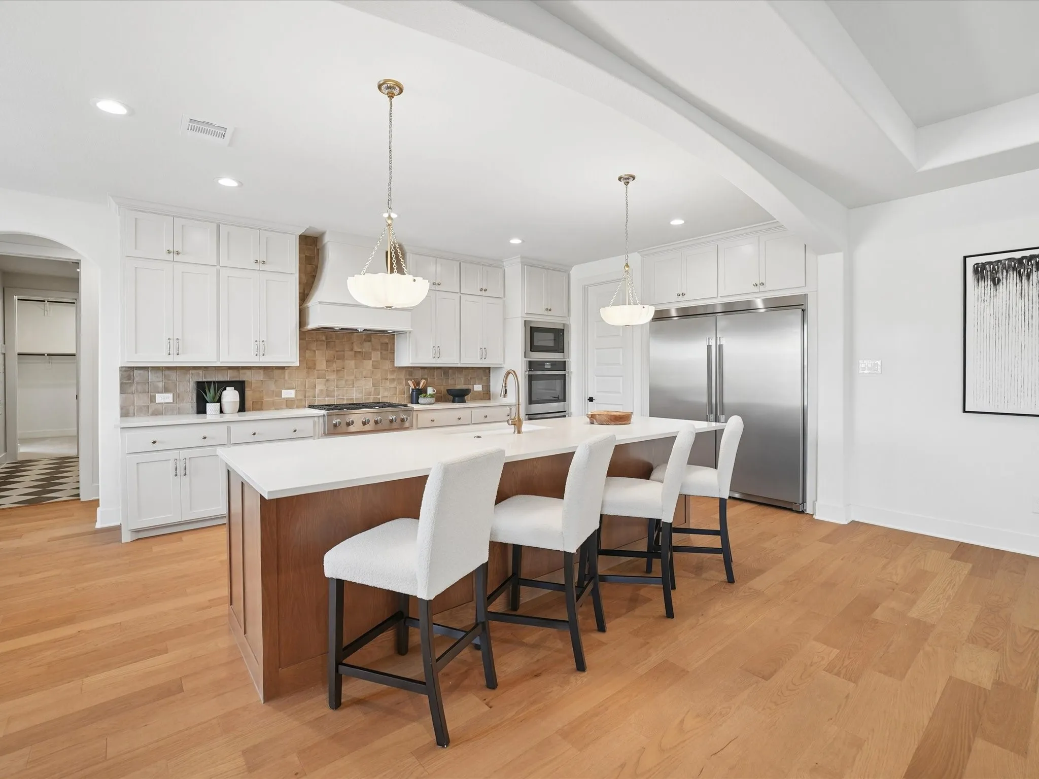 Hardwood flooring throughout, white cabinetry with gold-toned hardware, large center island with counter seating, stainless steel appliances, and ceiling beams