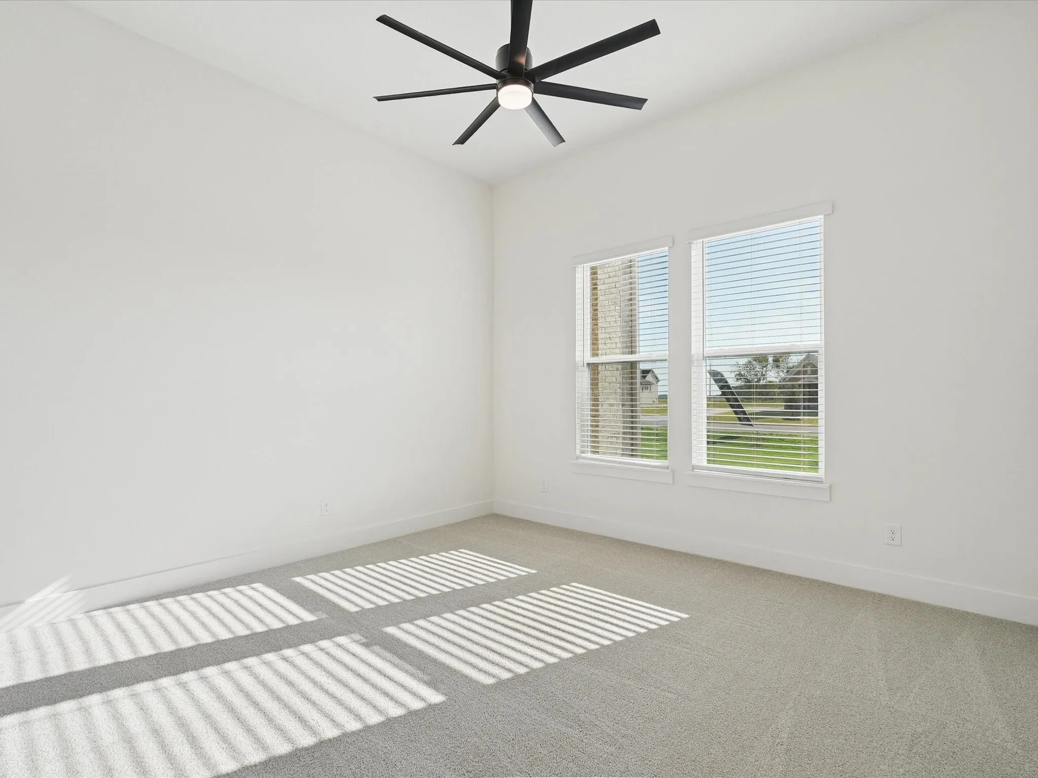Bright room featuring a ceiling fan, plush carpet, and dual windows with blinds