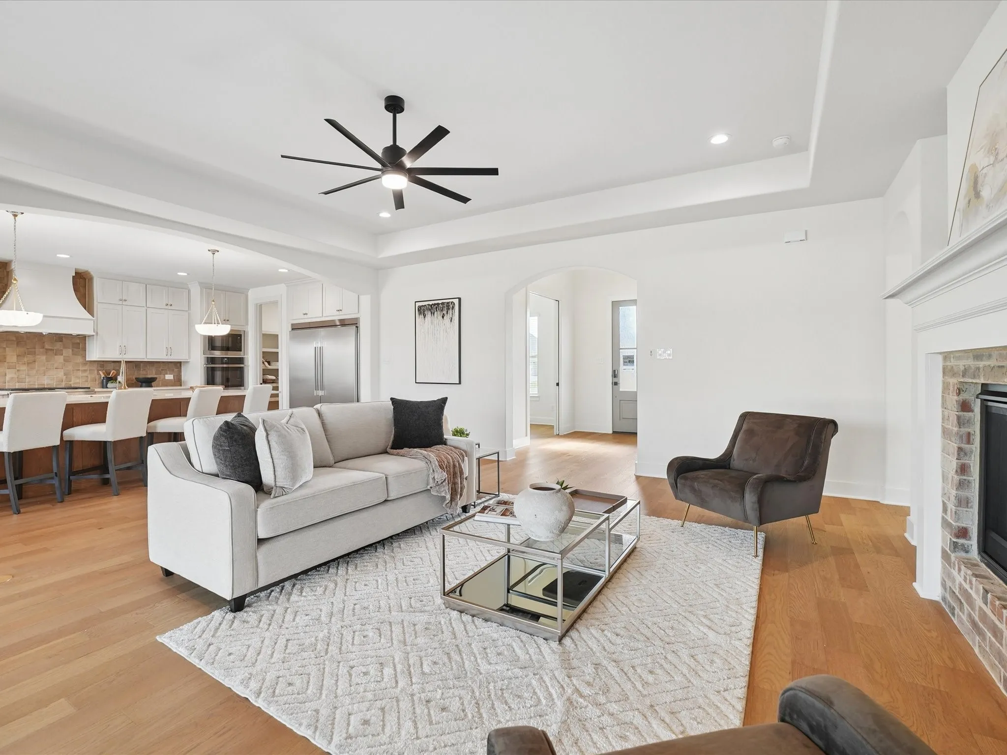 Recessed lighting, a modern ceiling fan, wood-finish flooring, a brick fireplace, and a tray ceiling