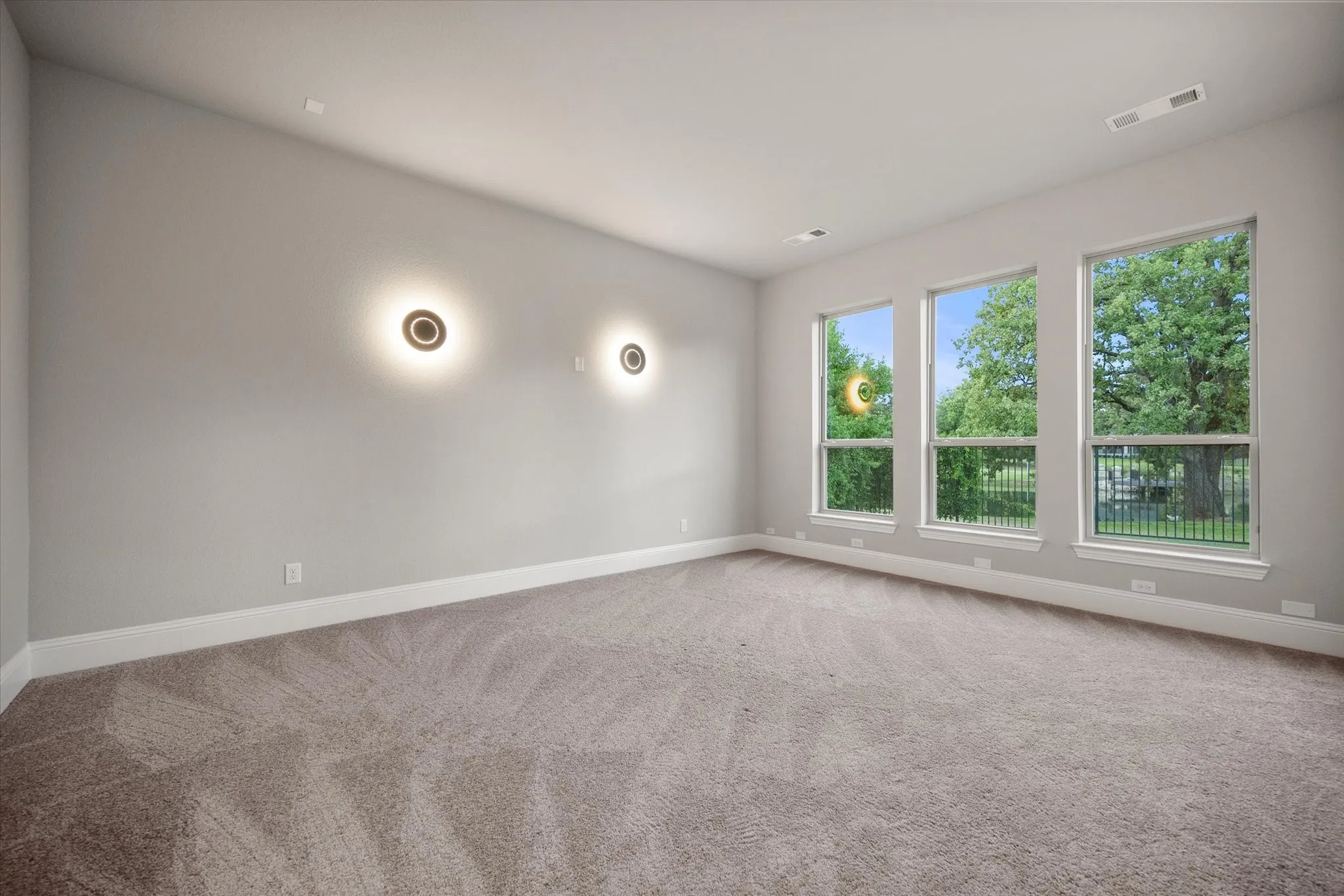 Spacious room featuring three large windows, neutral-toned carpeting, and two contemporary wall sconces