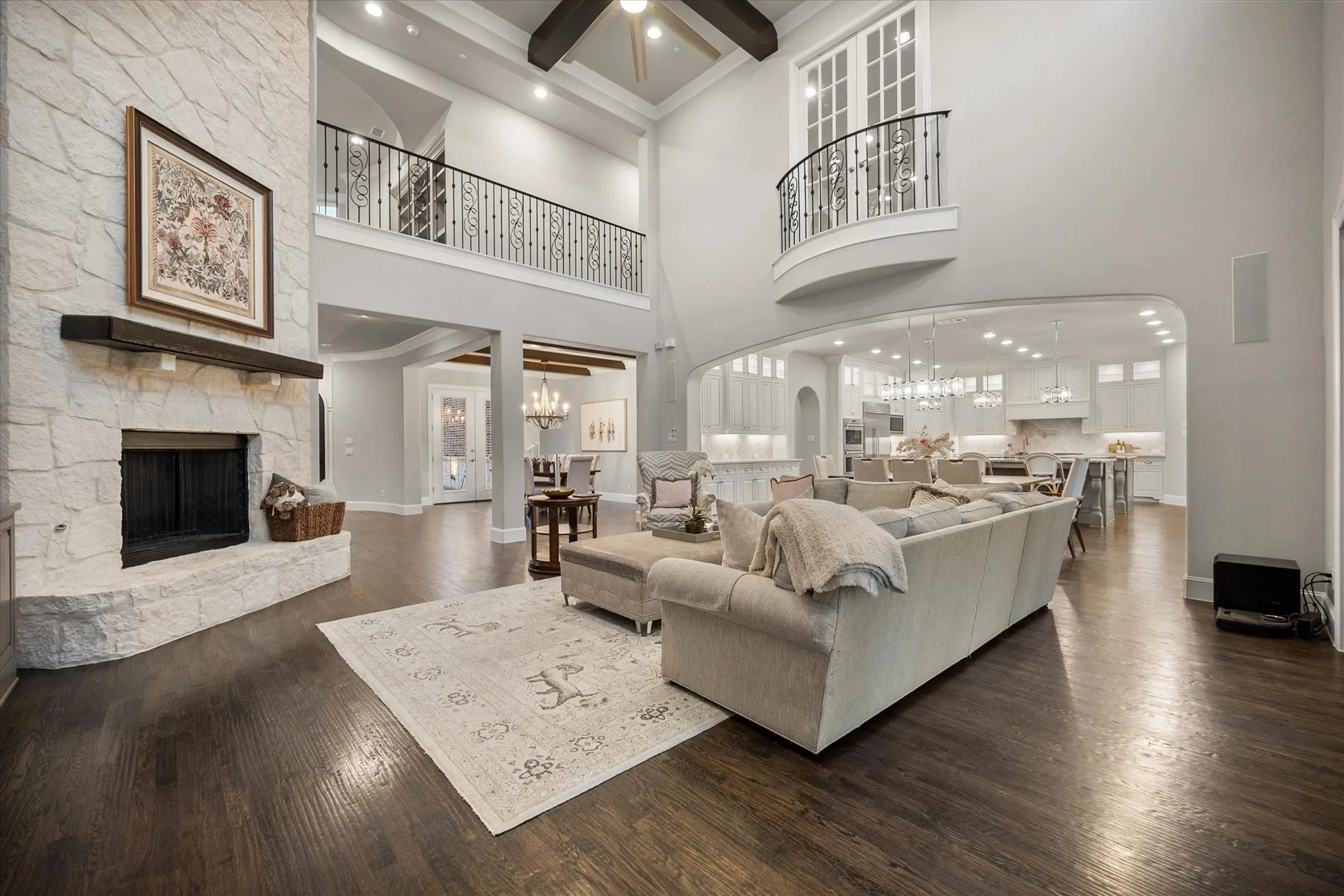 Stone-clad fireplace with a dark wood mantel, high ceilings, dark wood-finish flooring, an upper-level Juliet balcony, and a wrought iron railing