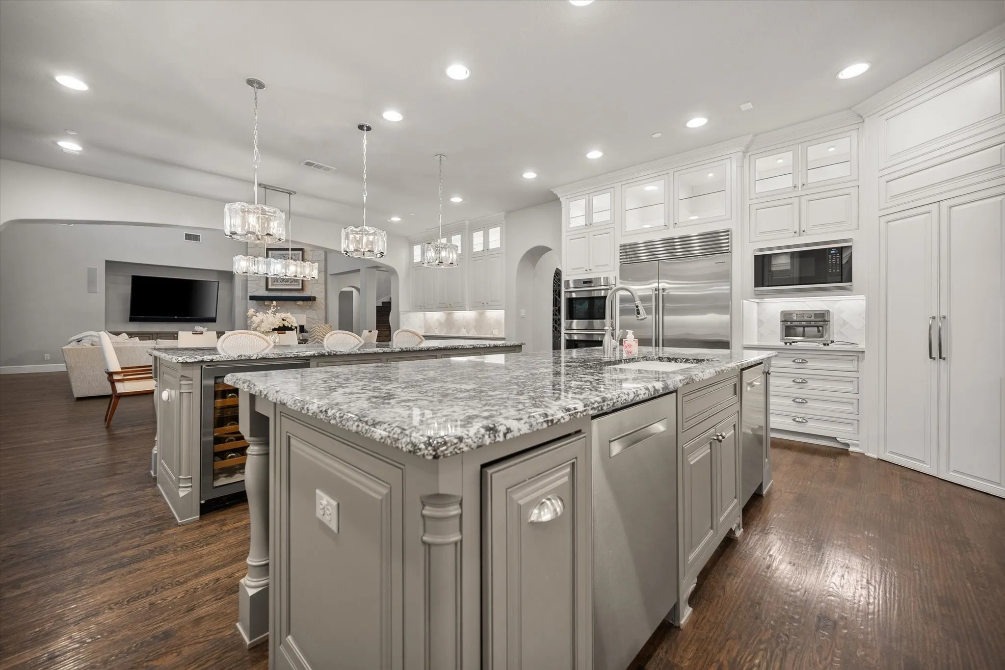 Gourmet kitchen featuring dual islands with stone countertops, stainless steel appliances, custom cabinetry, and wood-finish flooring