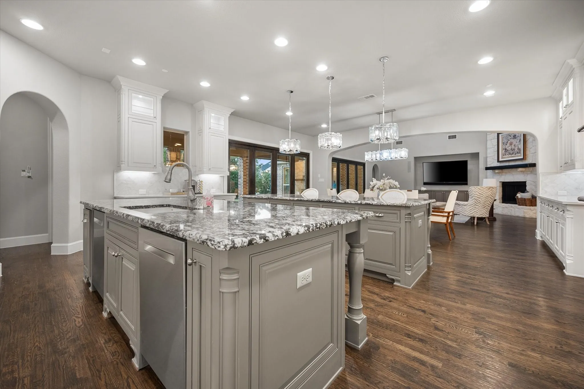 Dual kitchen islands with stone countertops, integrated stainless steel appliances, recessed lighting, and rich wood-finish flooring