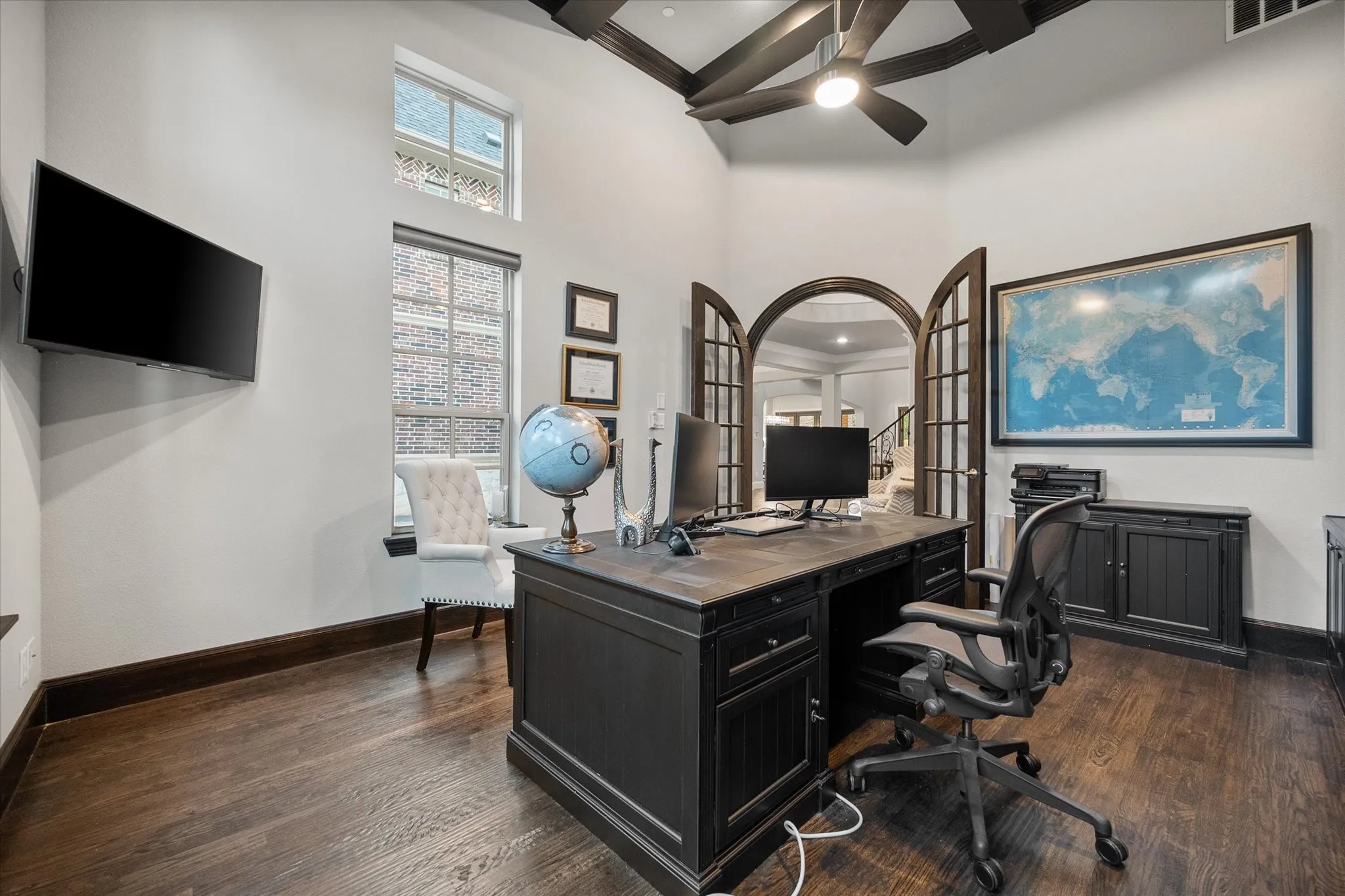 Hardwood flooring with dark trim, arched French doors, high ceilings with exposed beams, and a ceiling fan