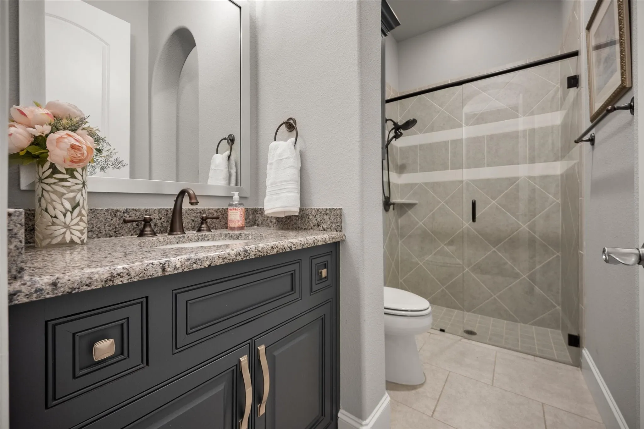 Dark gray vanity with brushed nickel hardware, granite countertop, undermount sink, and bronze-finish faucet