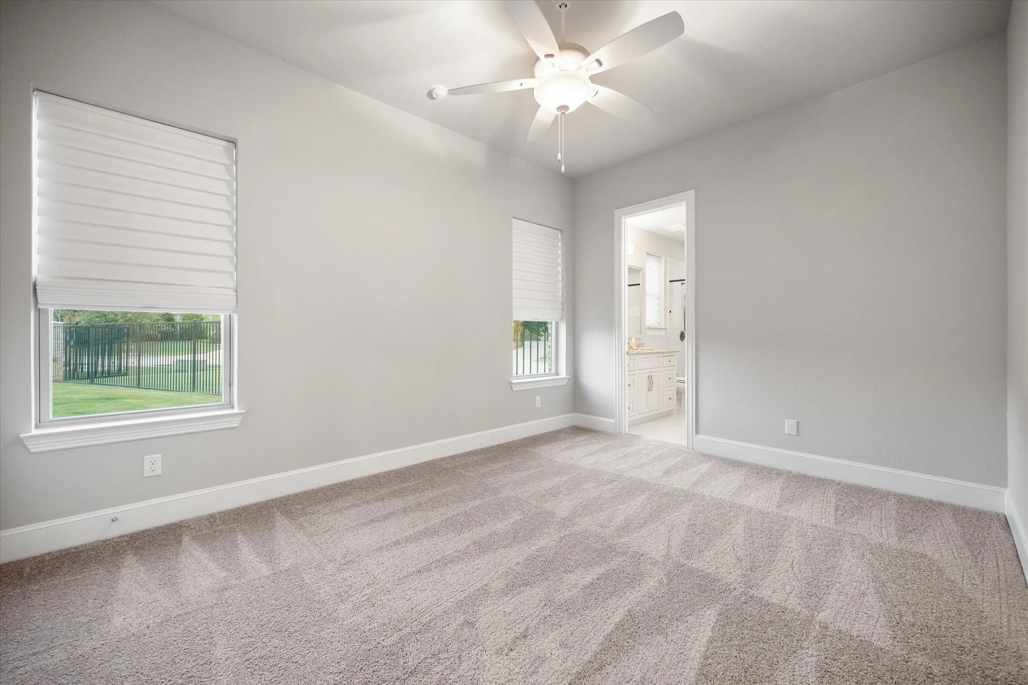 Neutral wall paint, plush carpet flooring, multiple windows, ceiling fan with integrated lighting, and an entryway to an adjoining bathroom