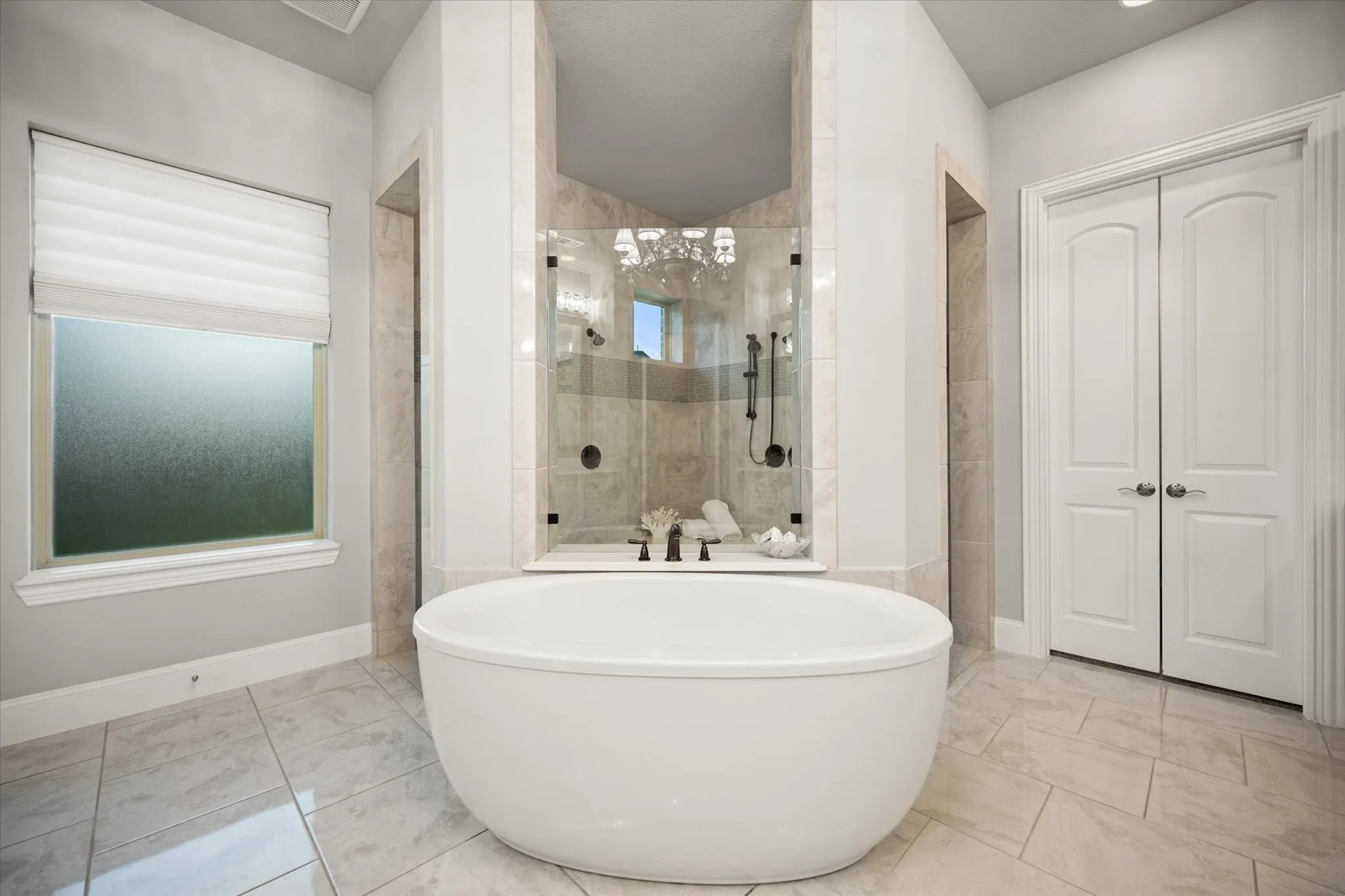 Freestanding soaking tub, tiled flooring, glass-enclosed shower, arched double doors, and a frosted privacy window