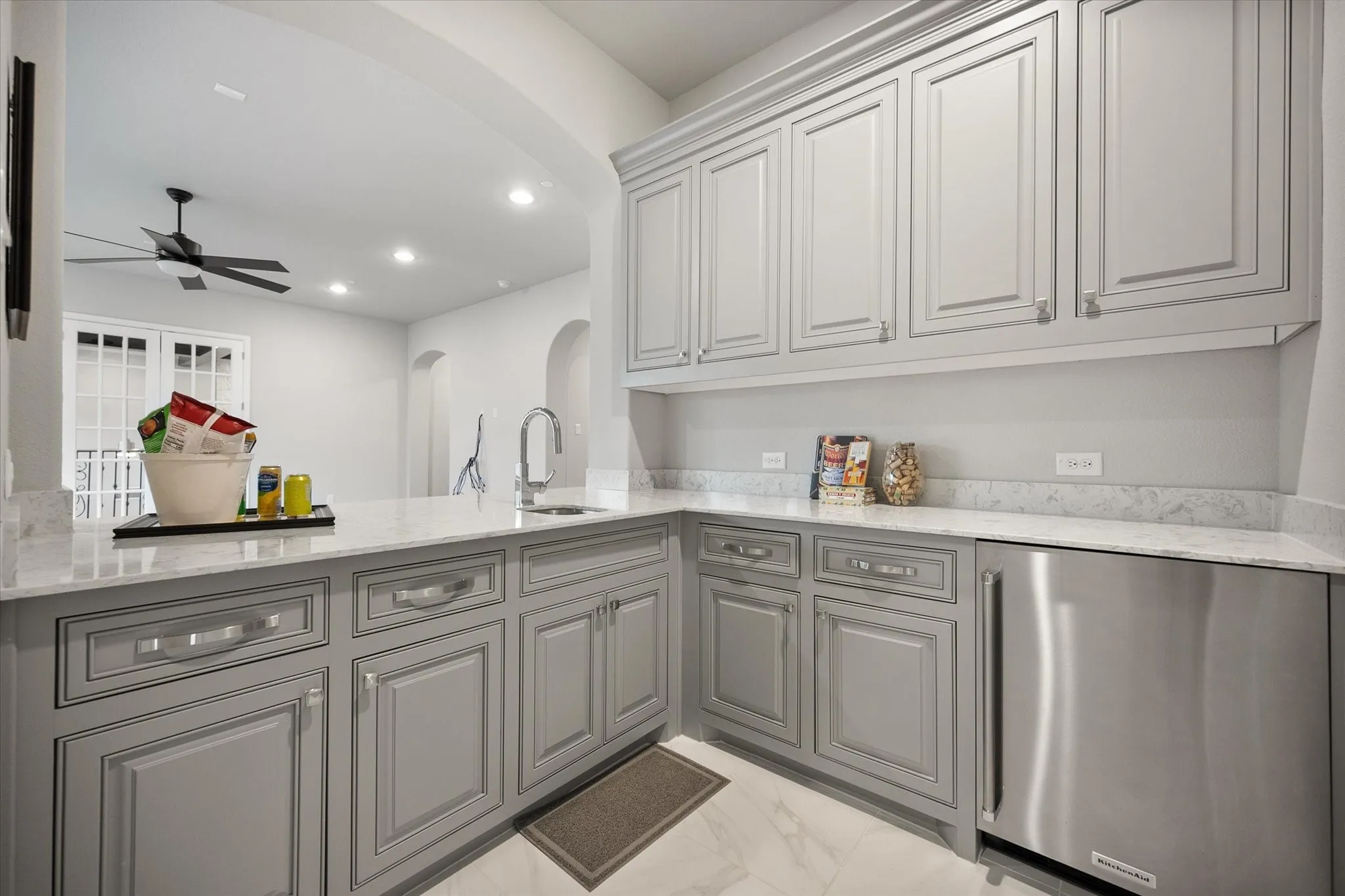 Wet bar featuring gray shaker-style cabinetry, a built-in stainless steel beverage refrigerator, and a white countertop with an undermount sink