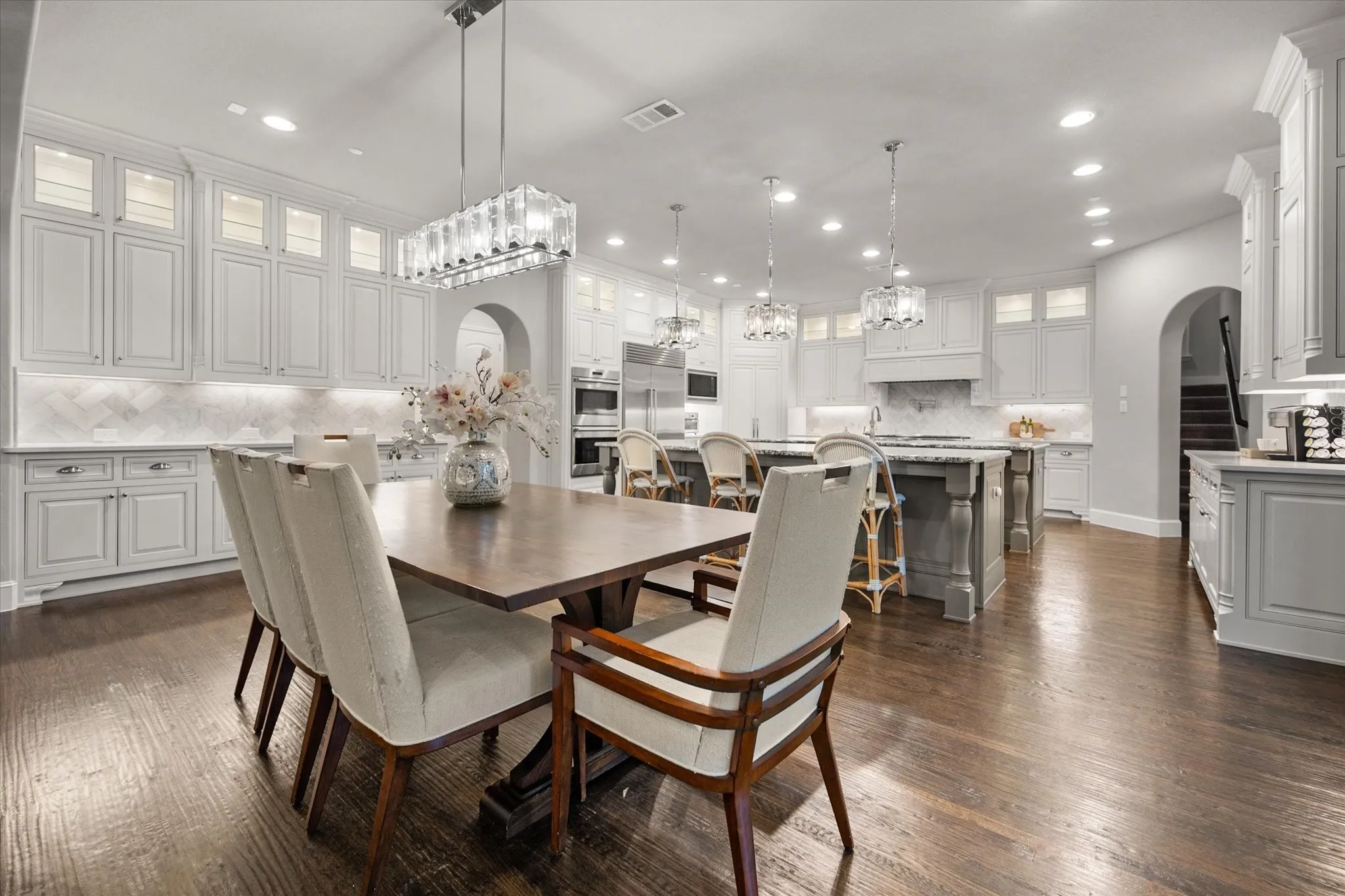 Expansive kitchen with wood-finish flooring, white cabinetry, integrated appliances, and recessed lighting