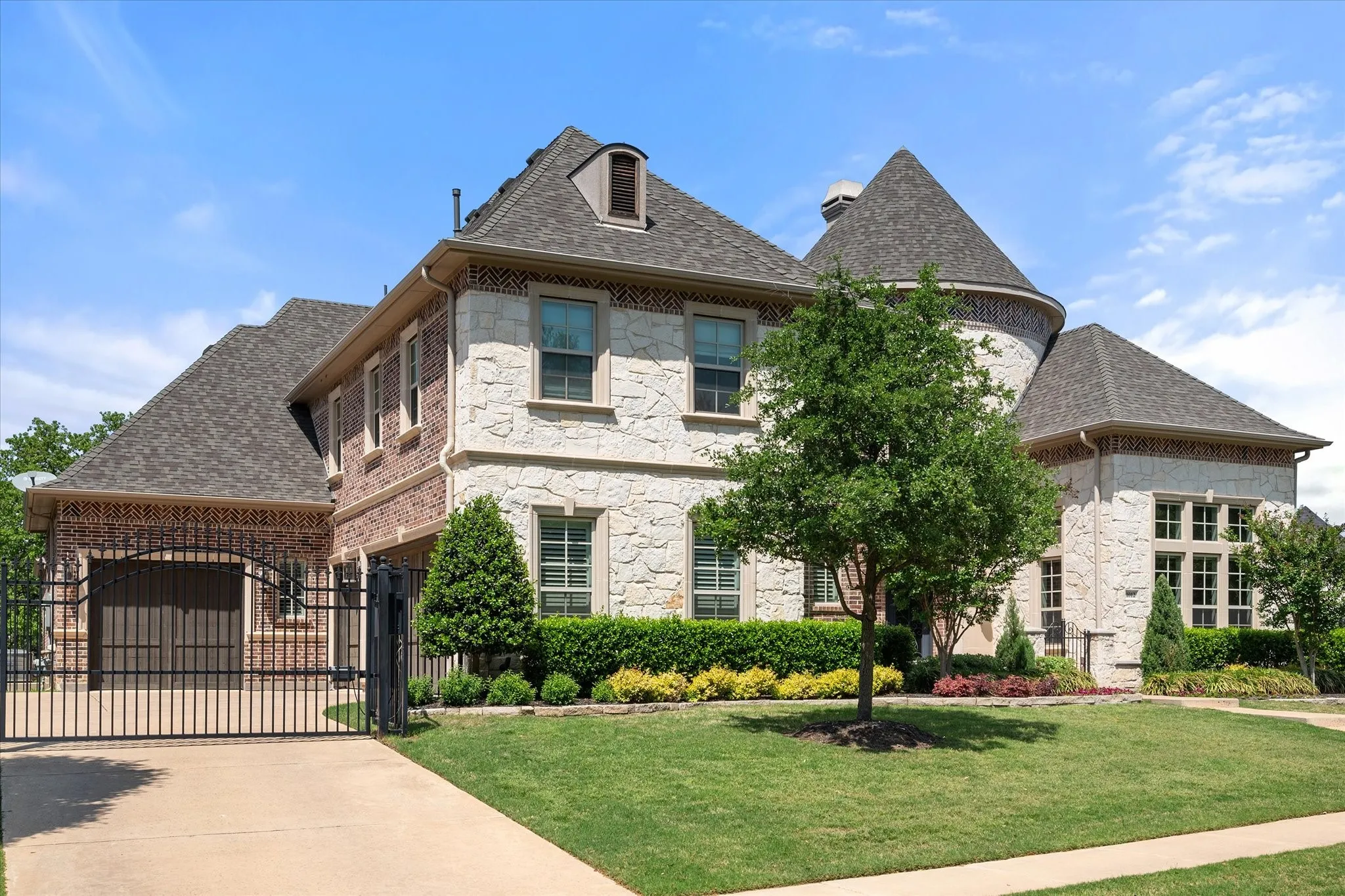 Stone and brick exterior with a turret, dormer window, and mature landscaping