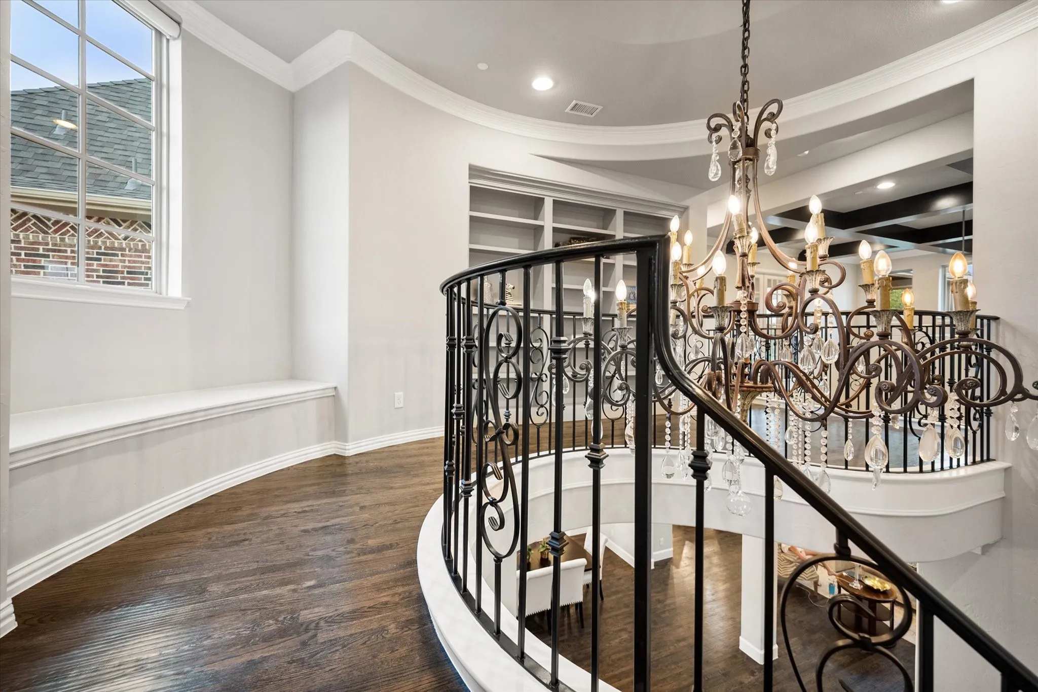 Curved hallway with rich wood-finish flooring, built-in window seating, and an ornate wrought iron and crystal chandelier