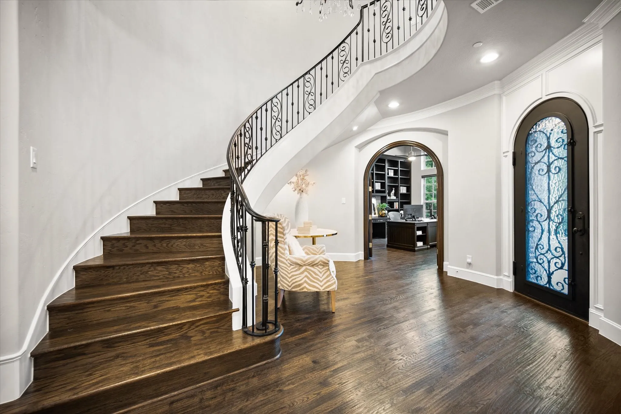 Grand curved staircase with dark wood treads and an ornate iron railing