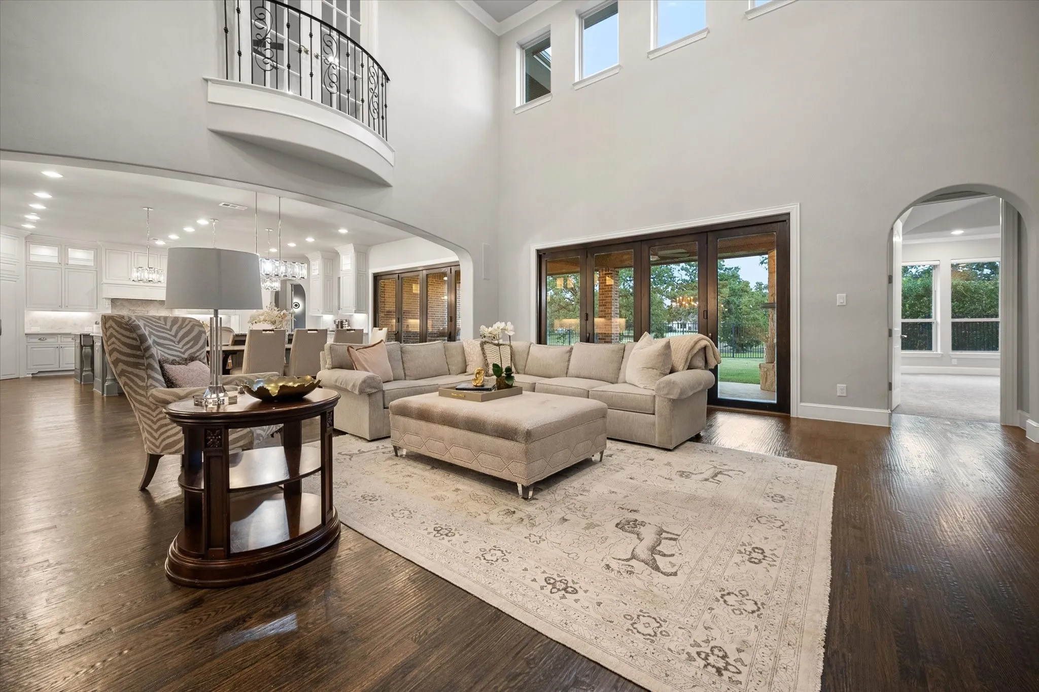 High ceilings featuring recessed lighting, dark wood-finish flooring, a second-story balcony with iron balustrades, large glass doors, and arched doorways
