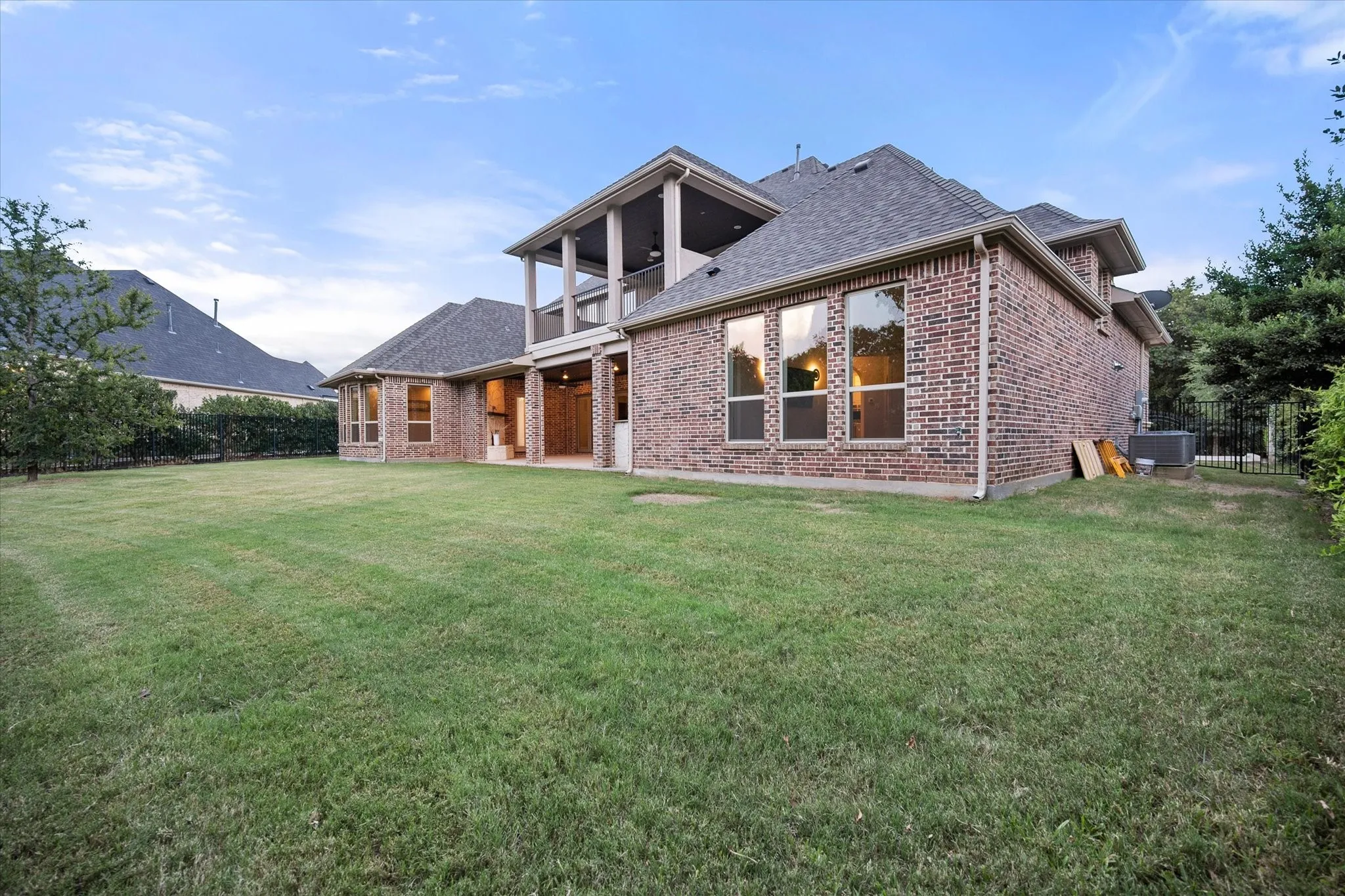 Brick exterior with multiple windows, covered patio, second-story balcony, and a spacious lawn