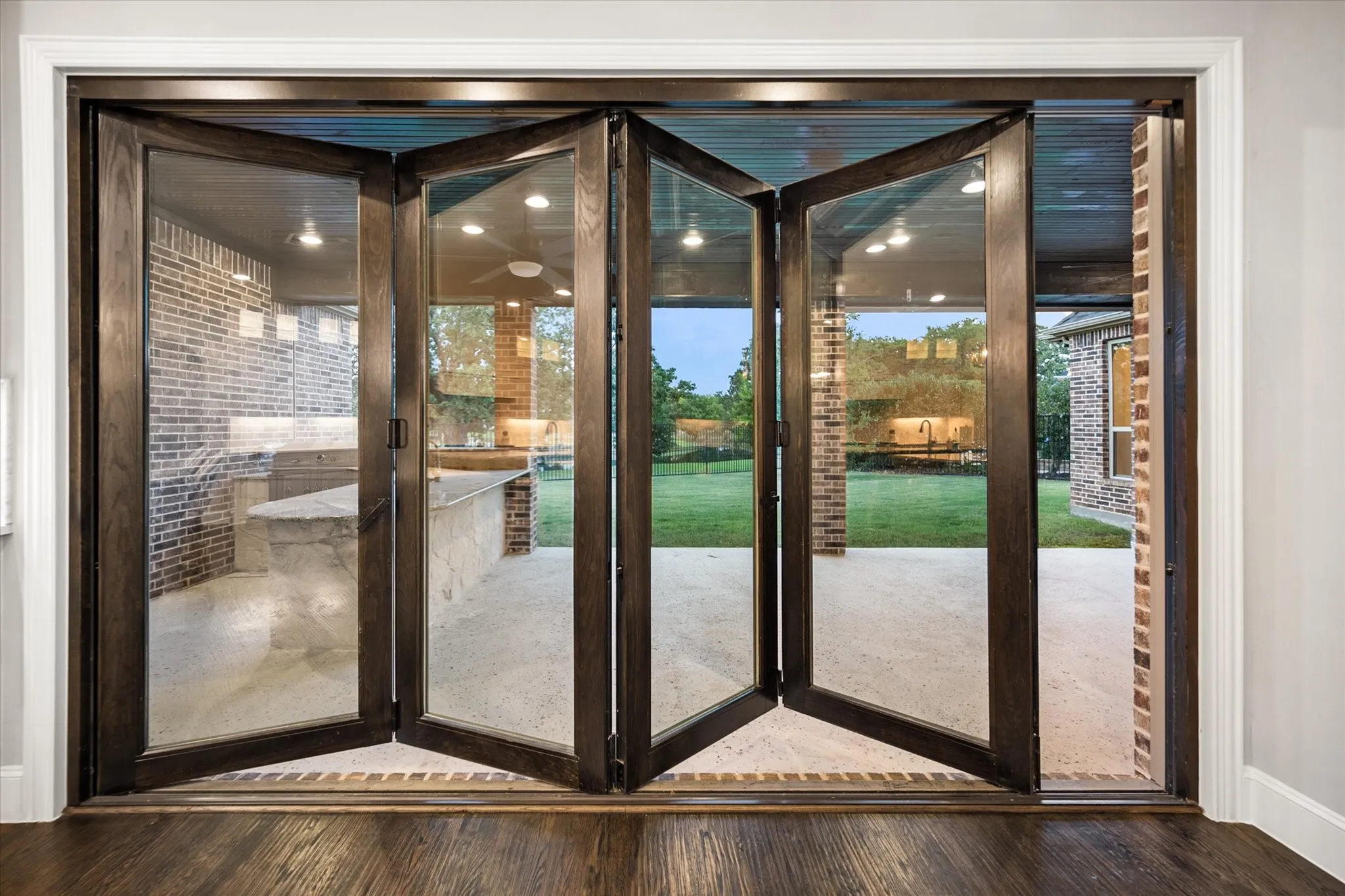 Bi-fold glass doors, concrete patio, built-in outdoor kitchen, brick exterior, and a manicured lawn