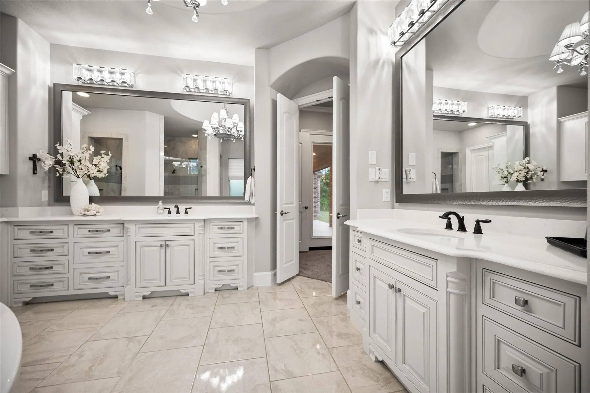 Dual vanity with white cabinetry and integrated sinks, oversized framed mirrors with overhead lighting, and tile flooring