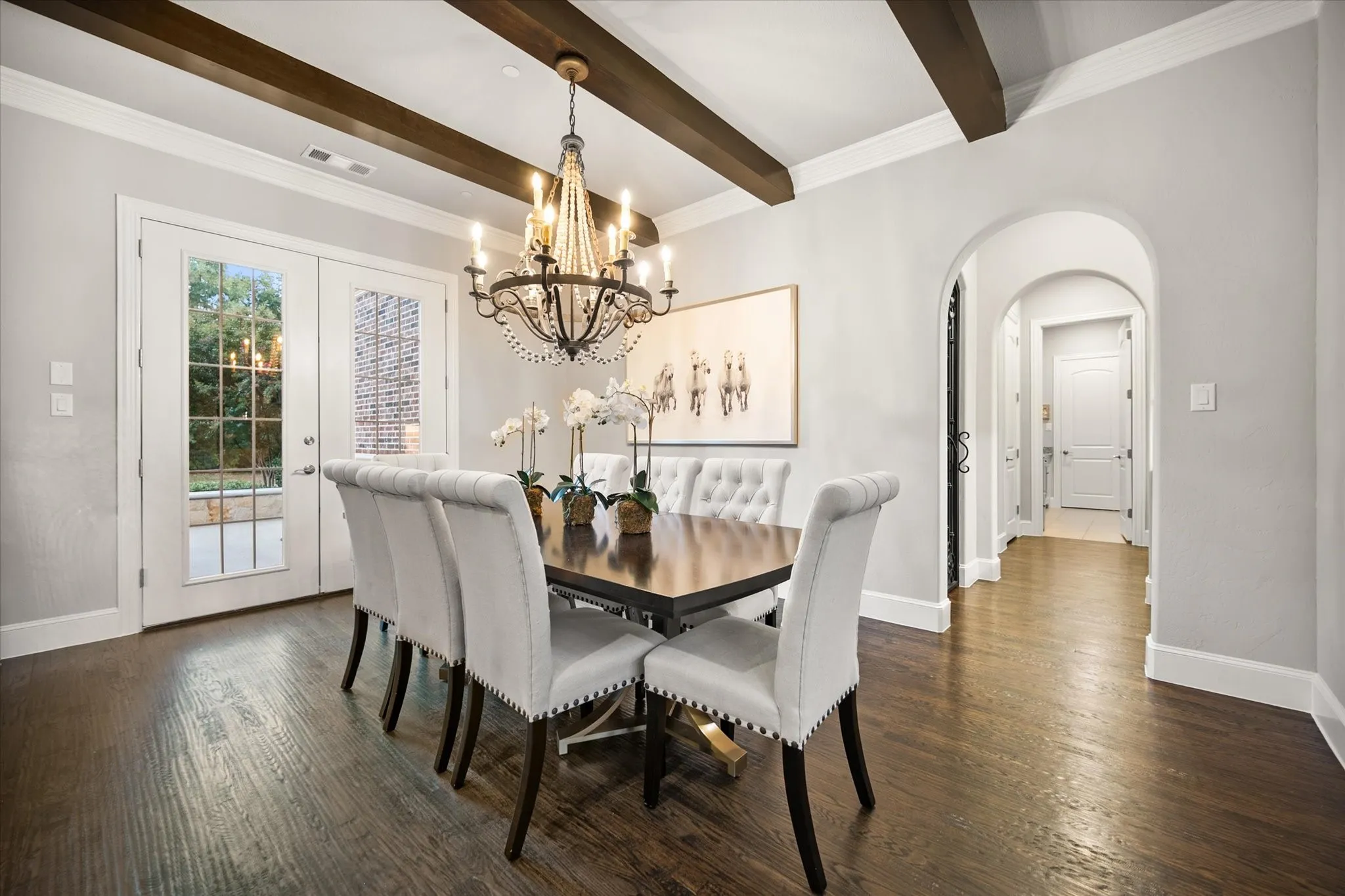 Hardwood flooring, exposed ceiling beams, decorative chandelier, French doors, and arched entryway