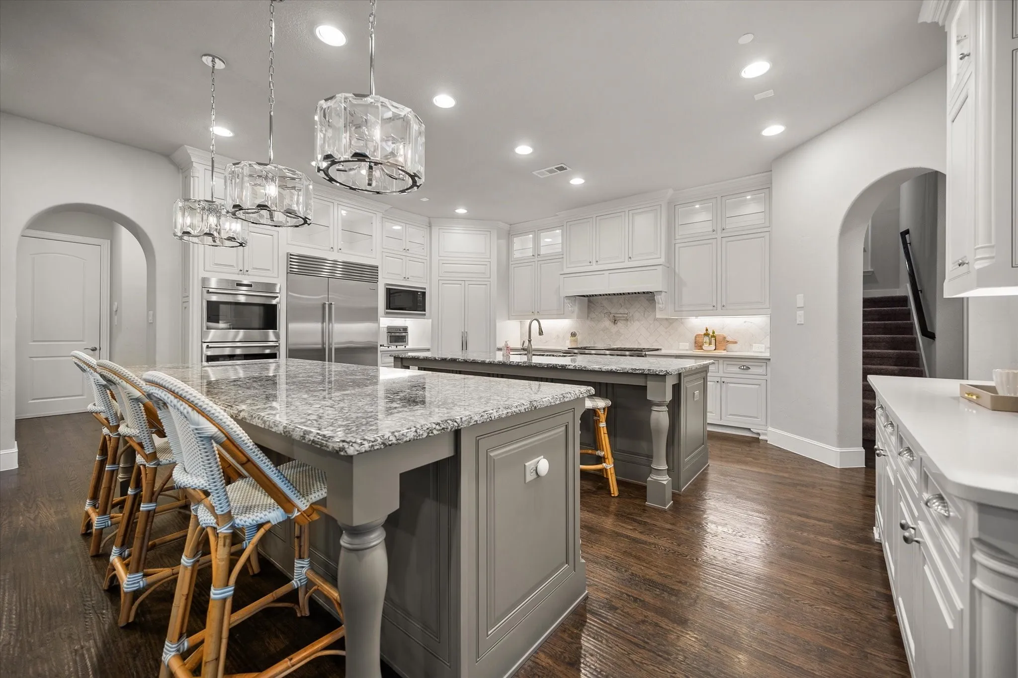 Gourmet kitchen featuring dual islands with stone countertops, stainless steel appliances, custom cabinetry, recessed lighting, and hardwood flooring