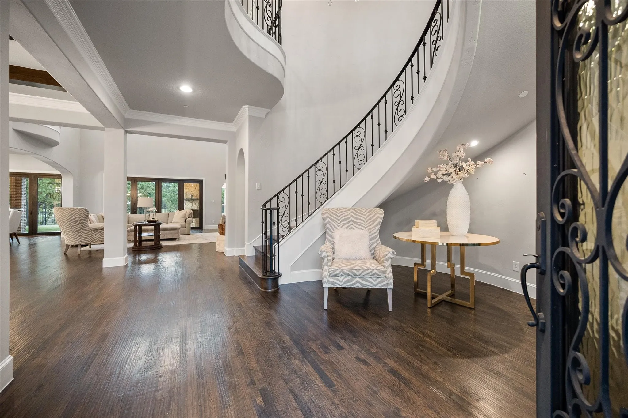 Grand entry featuring dark wood-finish flooring, a curved staircase with wrought iron balusters, recessed lighting, and a decorative front door with iron scrollwork