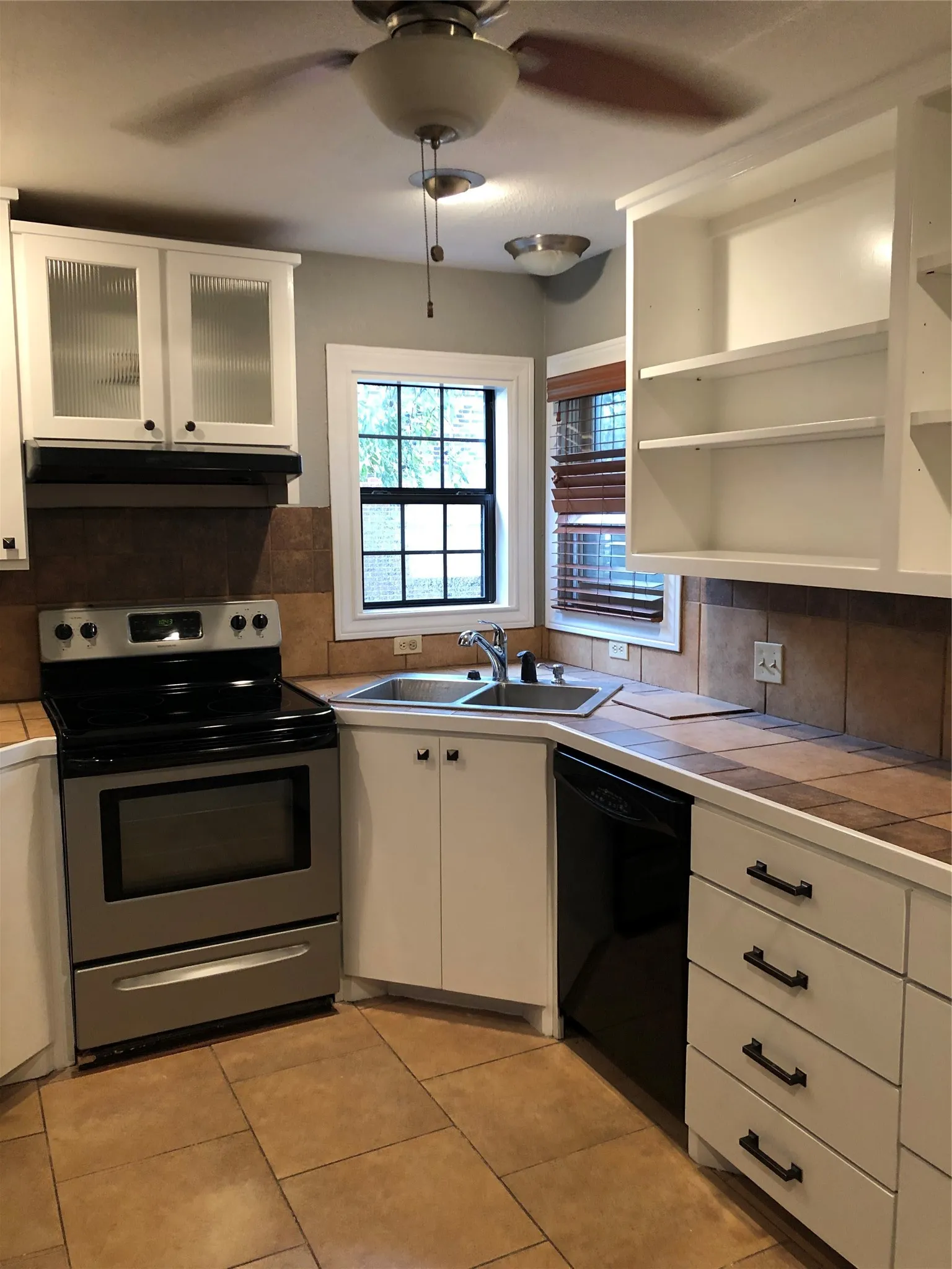 Kitchen with tile counters, dishwasher, ceiling fan, decorative backsplash, and stove