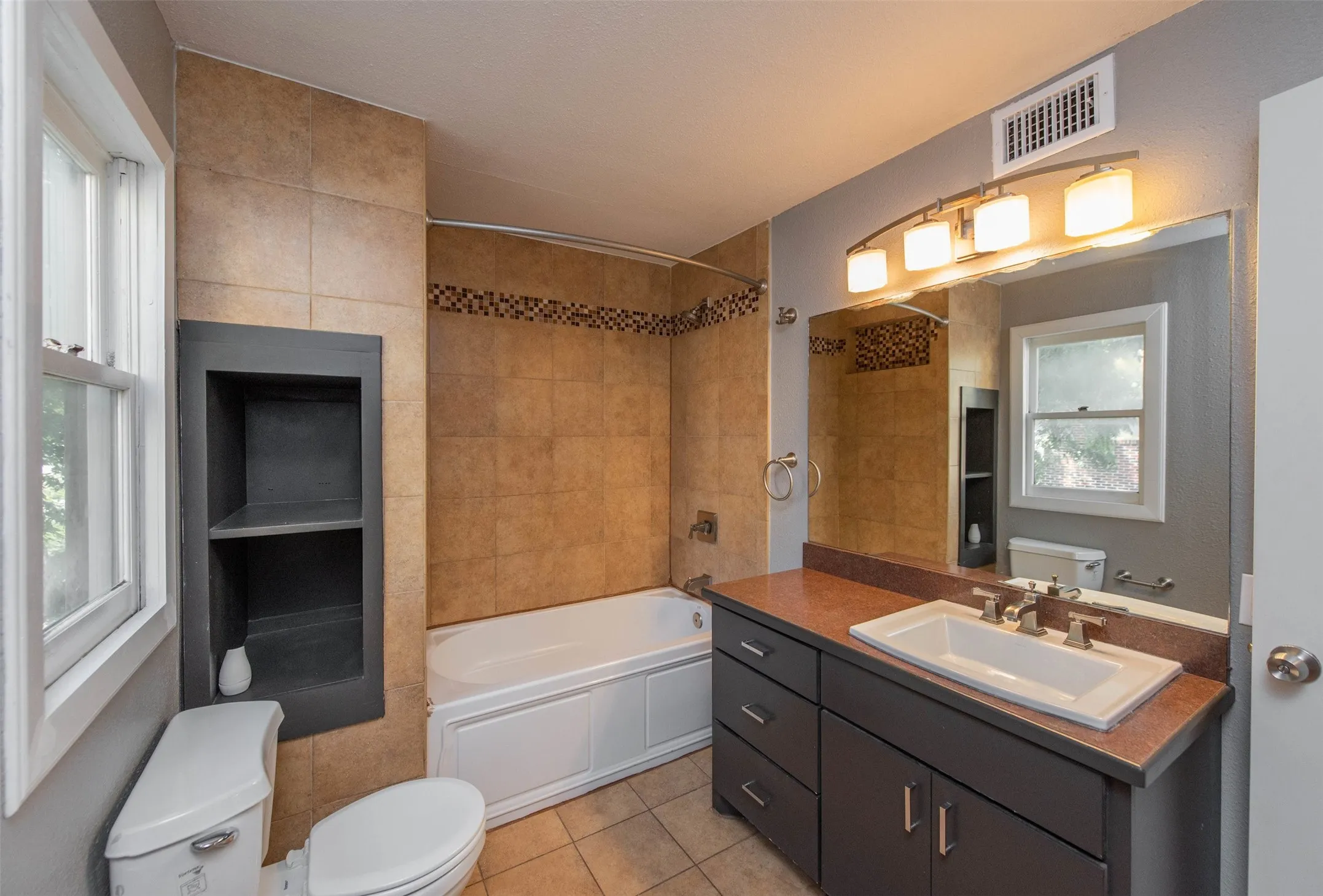 Full bathroom with tile patterned floors, toilet, vanity, and tiled shower / bath