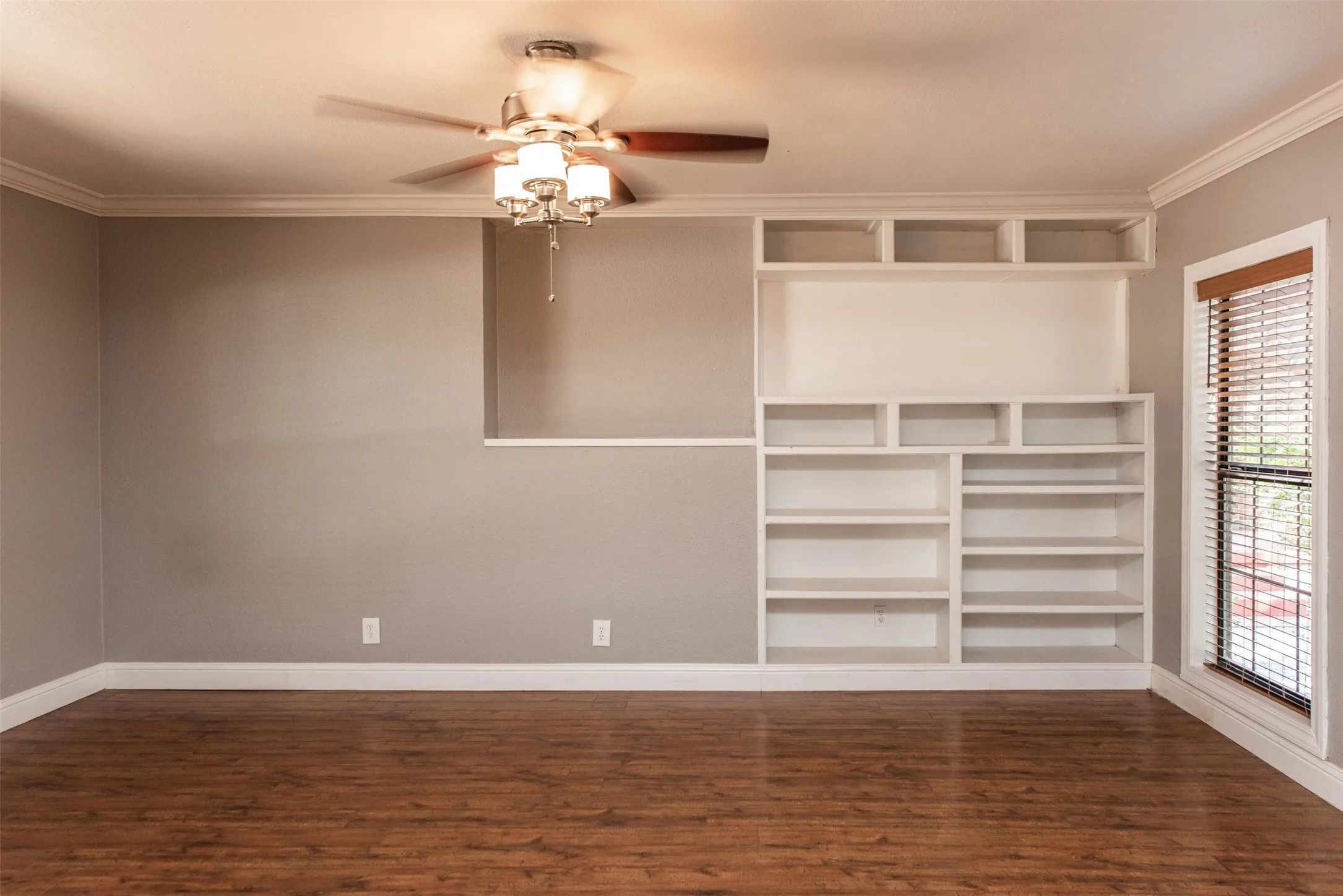 Unfurnished living room featuring dark wood-type flooring, ceiling fan, and ornamental molding