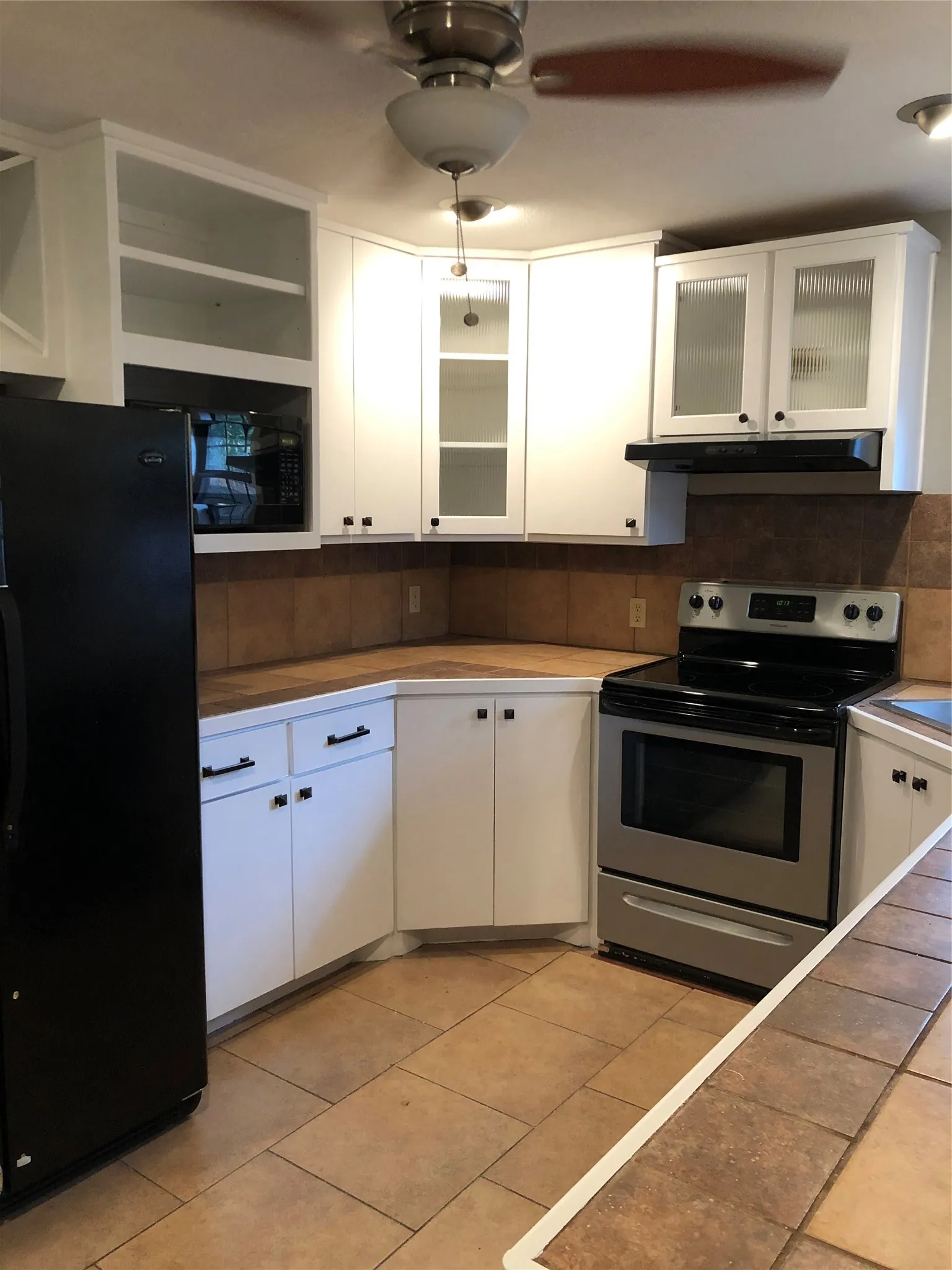 Kitchen featuring range, ventilation hood, fridge, light tile patterned flooring, and ceiling fan