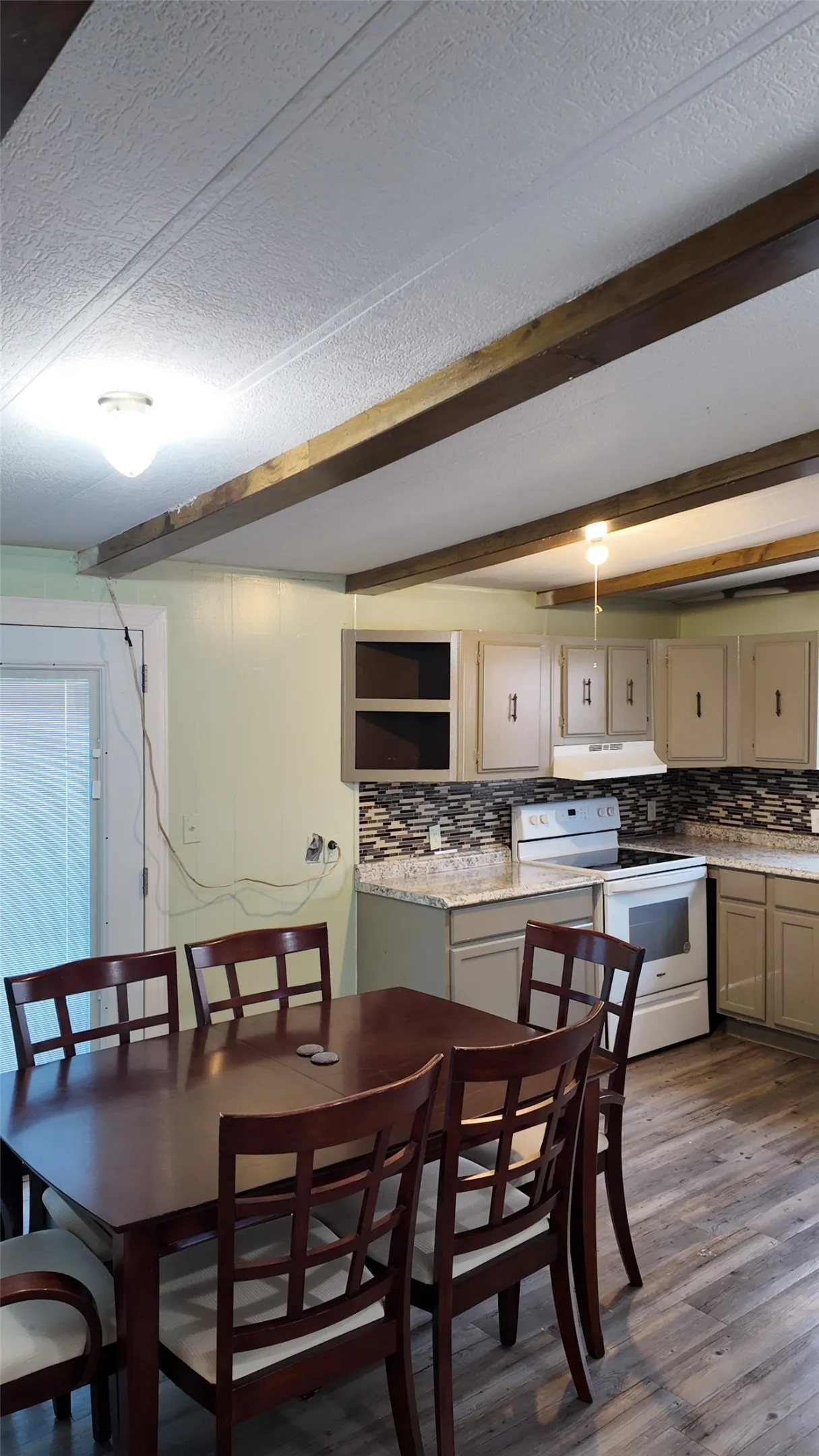 Wood-finish flooring, exposed ceiling beams, light-toned cabinetry, patterned tile backsplash, and light-colored countertops
