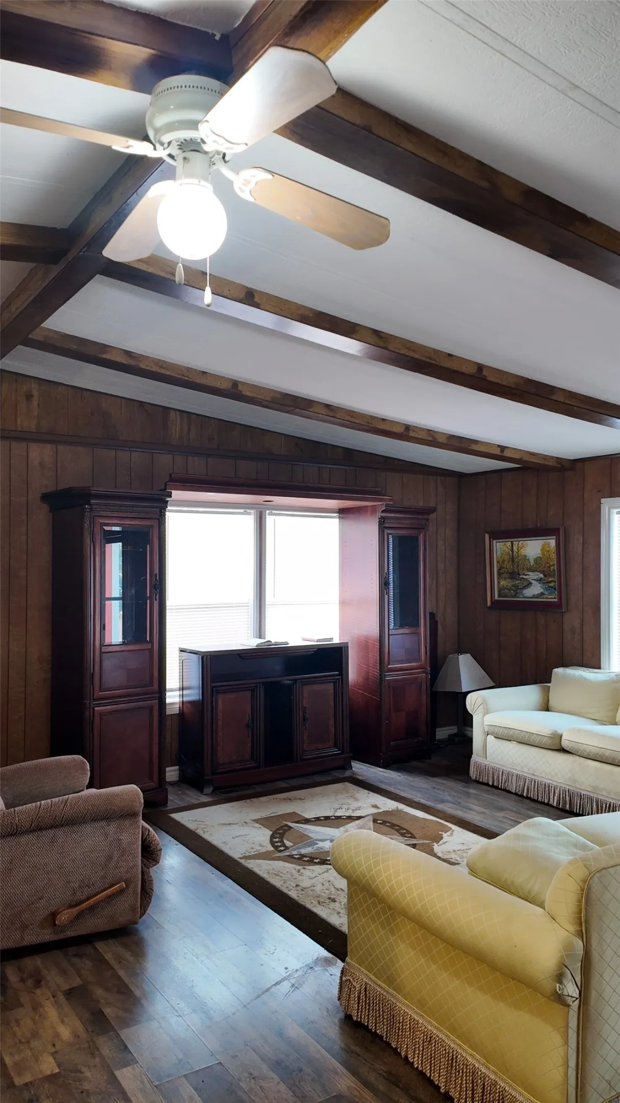 Wood-finish flooring, paneled walls, exposed wood beams, and a ceiling fan with integrated lighting