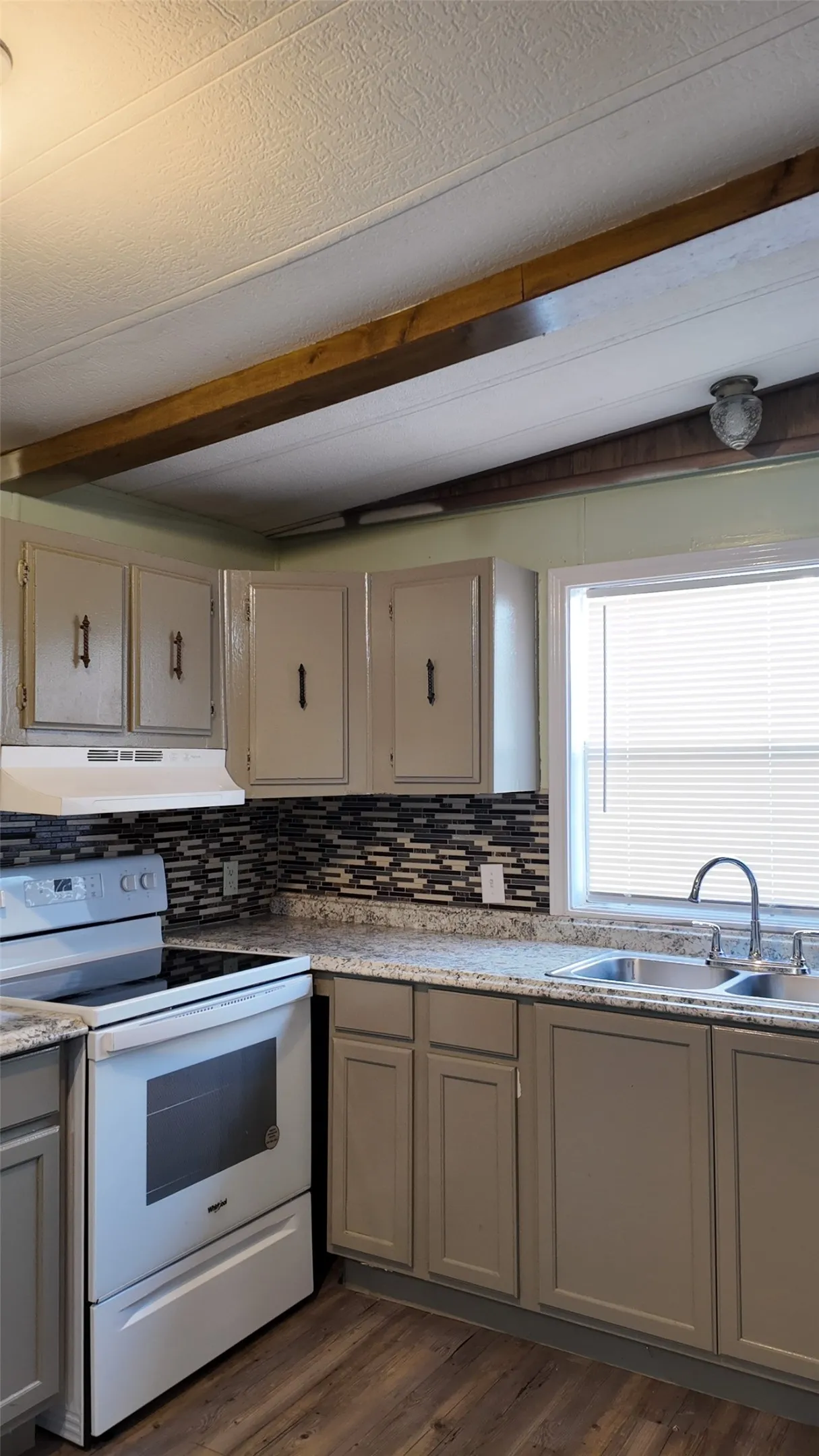 Kitchen with wood-finish flooring, light cabinetry, a mosaic tile backsplash, and a double basin sink