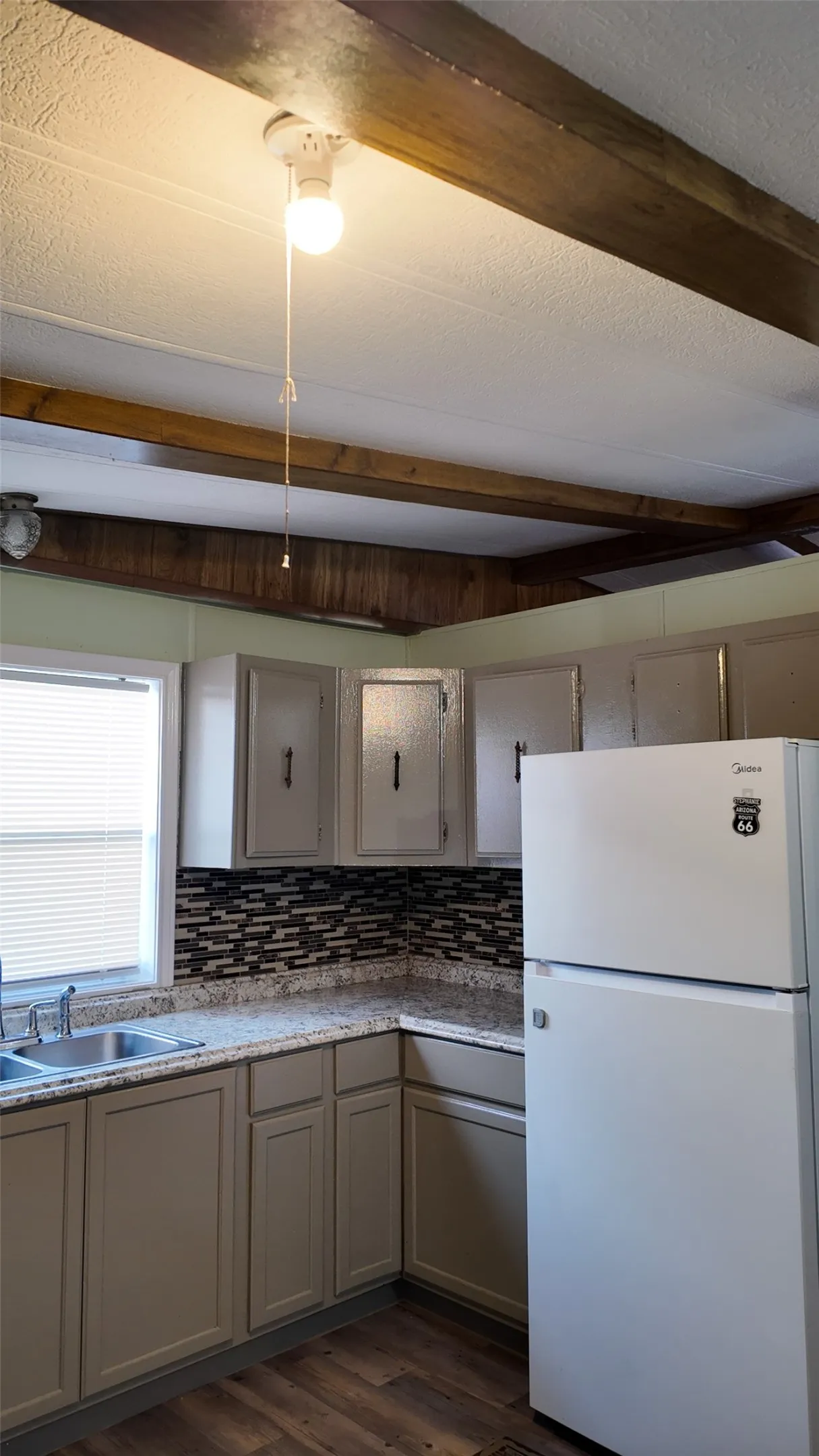 Kitchen featuring wood-finish flooring, two-tone cabinetry, mosaic tile backsplash, and a double basin sink