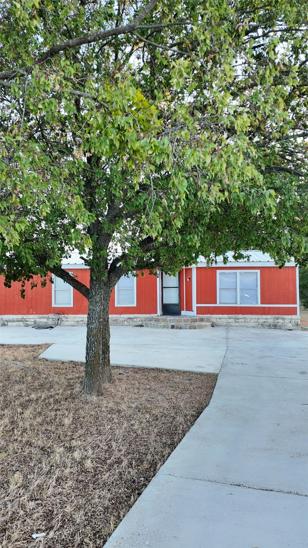 Red exterior siding with white trim, stone foundation, and a concrete driveway