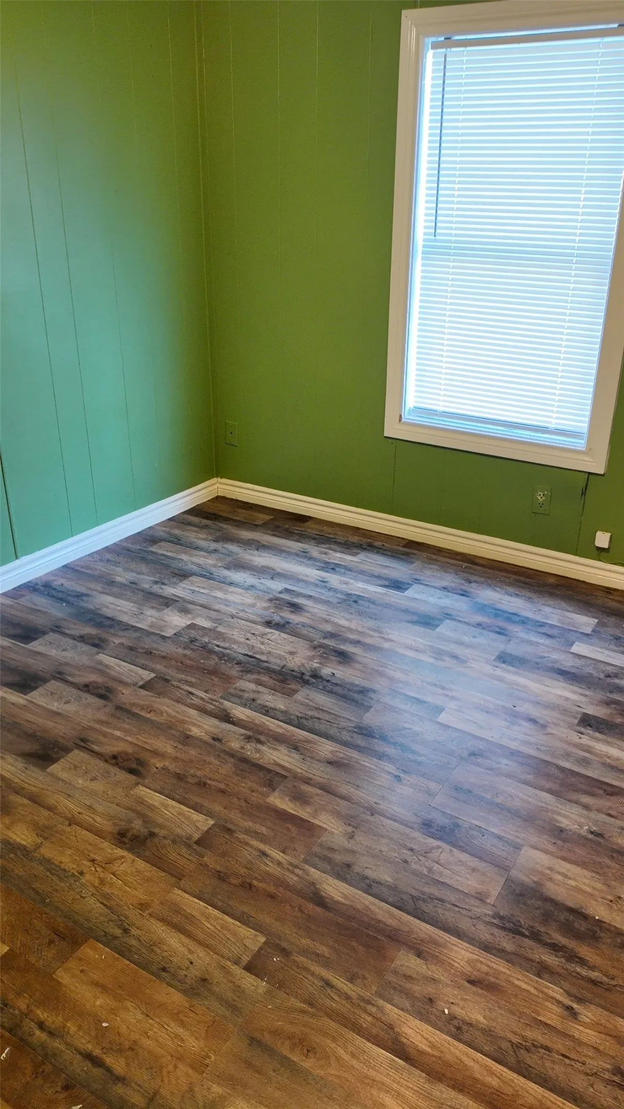 Wood-finish flooring with white trim and a window with blinds