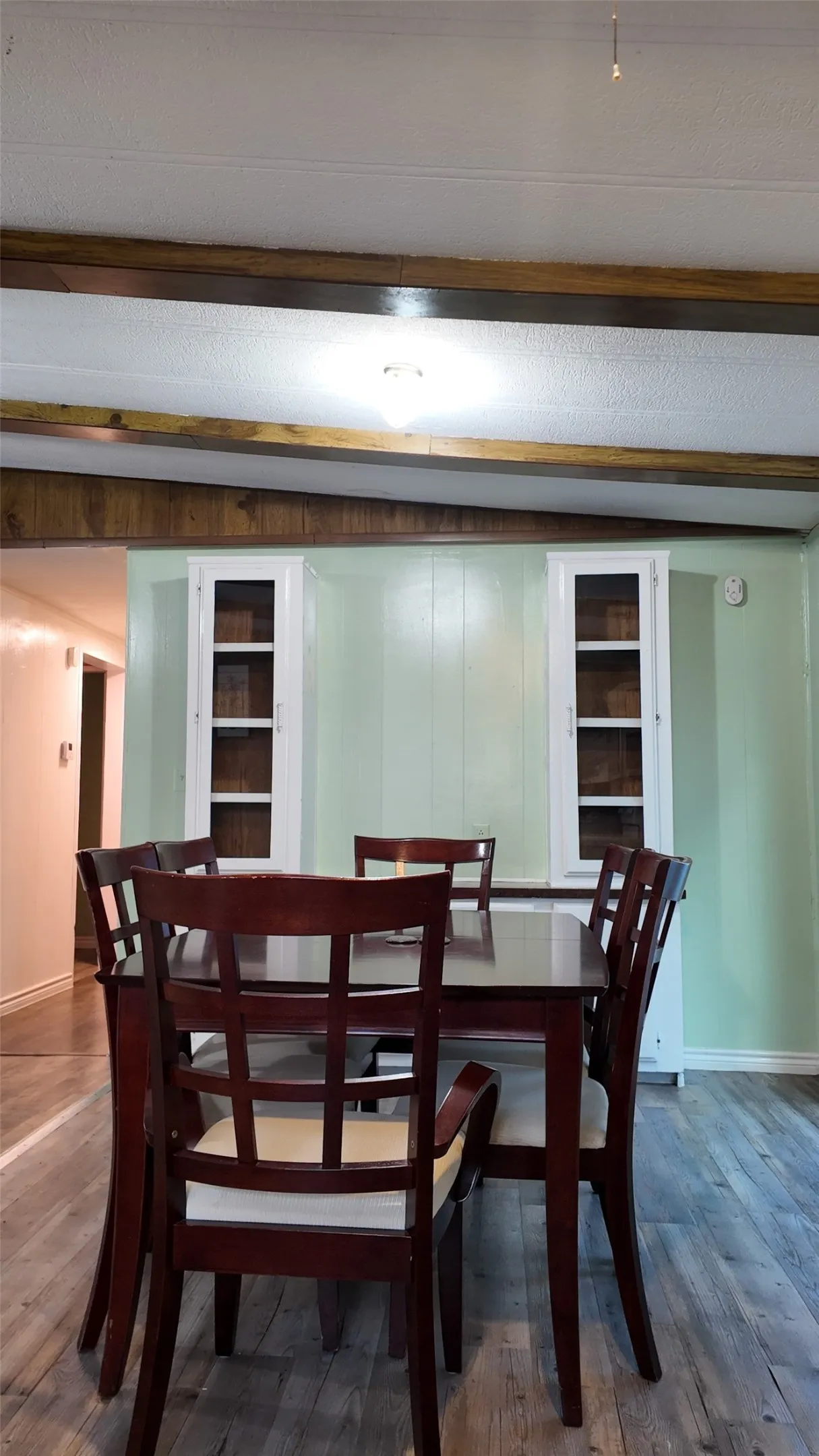 Wood-finish flooring, two built-in glass-front cabinets, and exposed wood ceiling beams