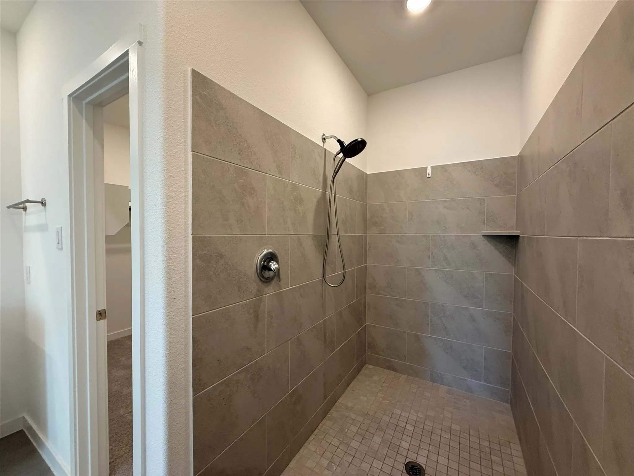 Tiled shower with a rainfall showerhead, handheld shower fixture, and a built-in shelf