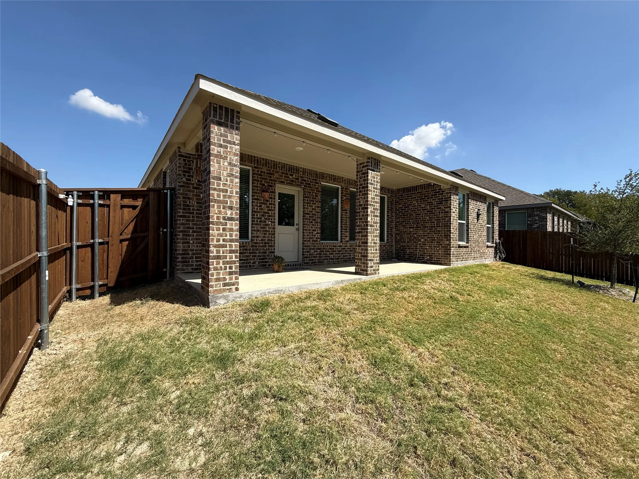 Brick exterior with covered patio, wood fencing, and a sloped lawn