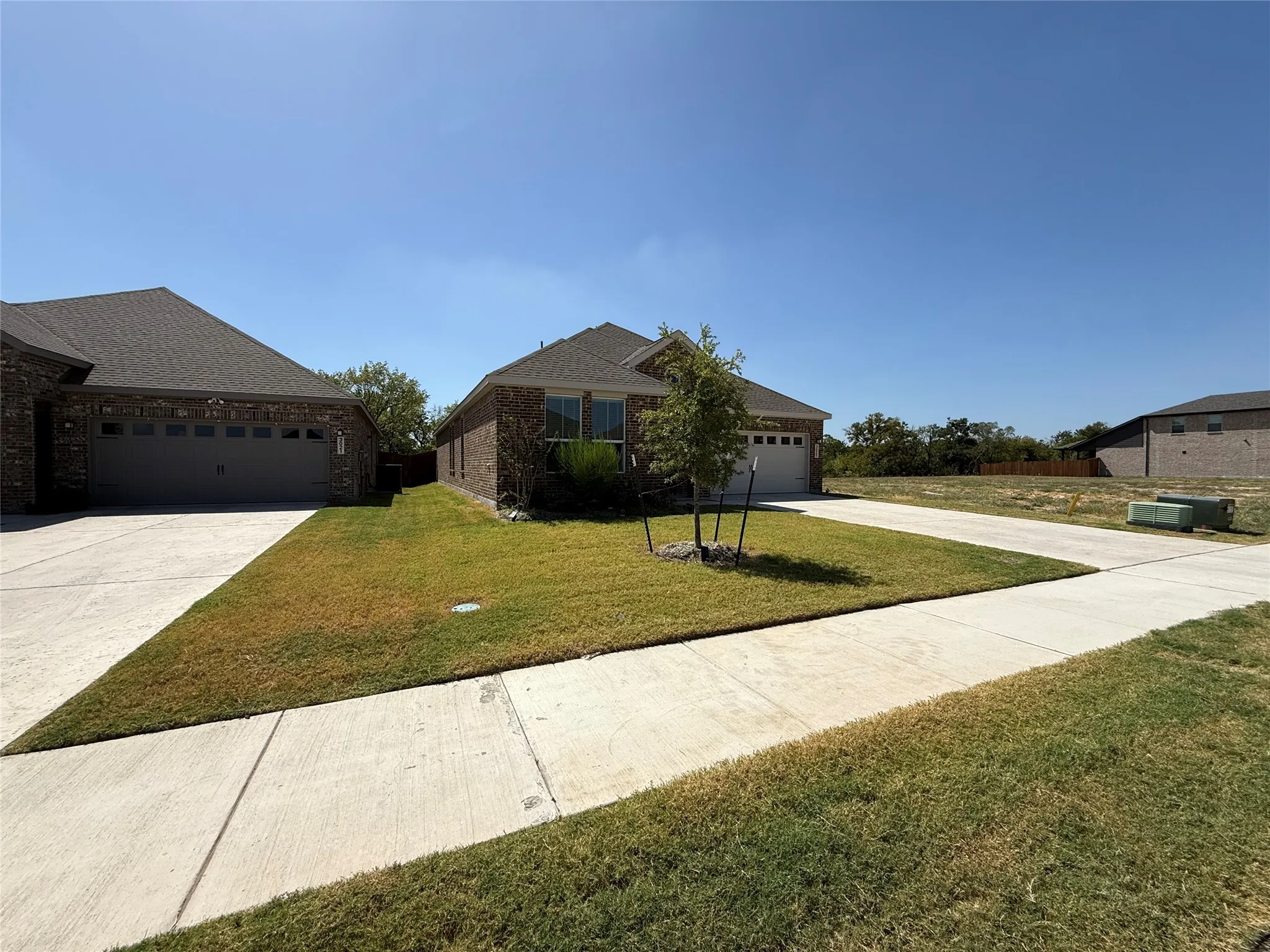 Brick exterior with an attached two-car garage, concrete driveway, and a front yard with established landscaping