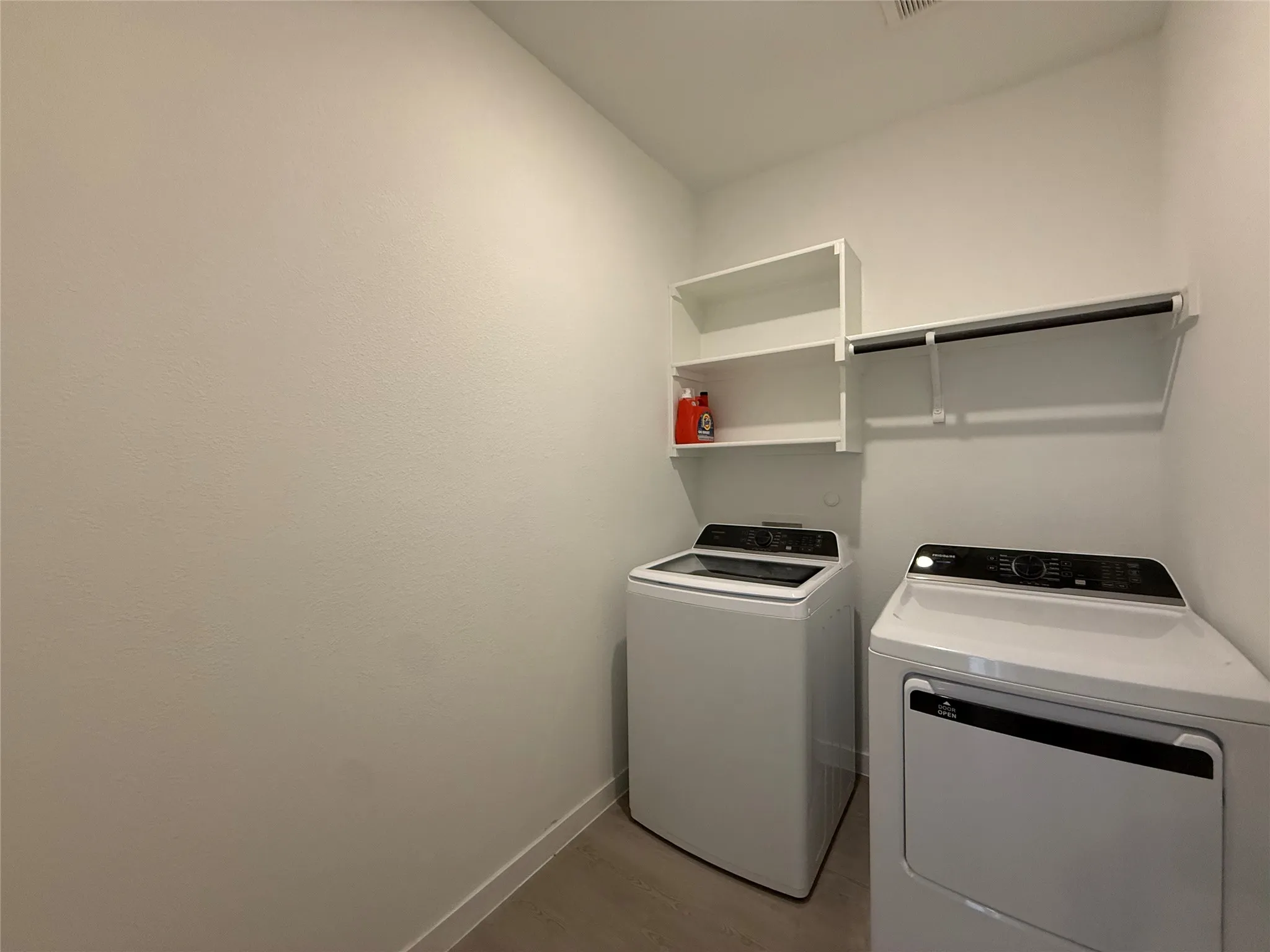 Dedicated laundry area featuring built-in white shelving, a clothing rod, and wood-finish flooring