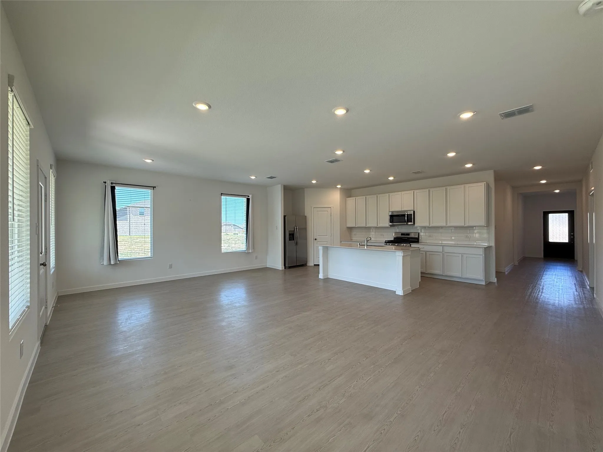Open-concept living space featuring wood-finish flooring, recessed lighting, and a kitchen with white cabinetry, a center island, and stainless steel appliances