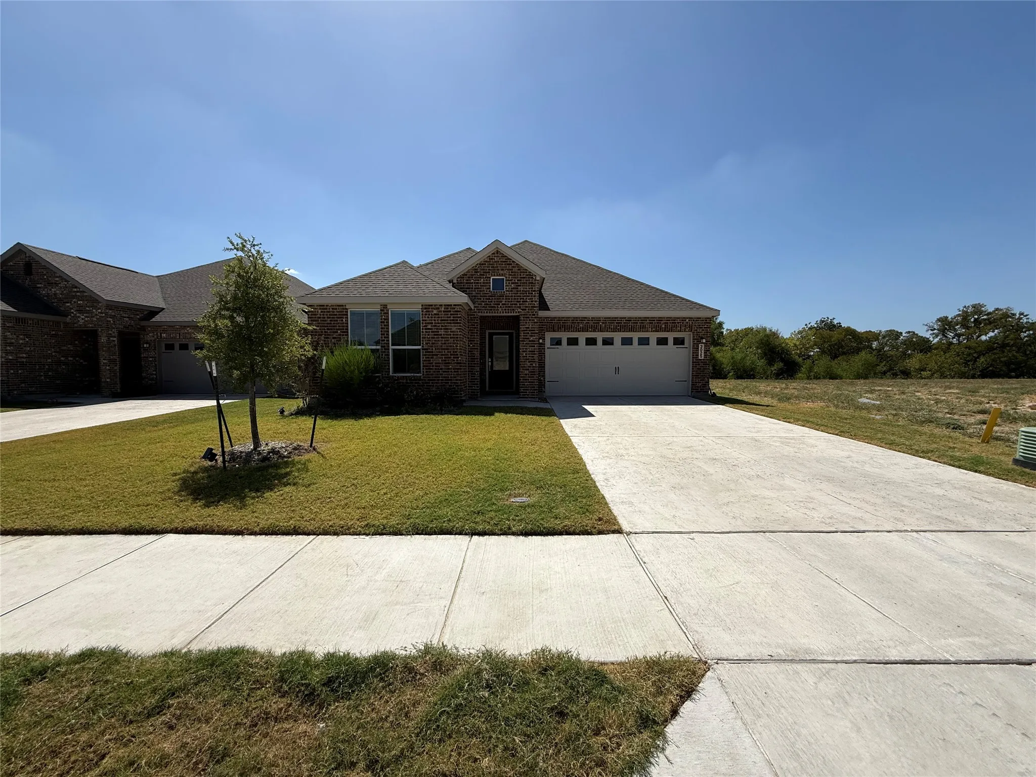 Brick exterior with an attached garage, paved driveway, and established front yard landscaping
