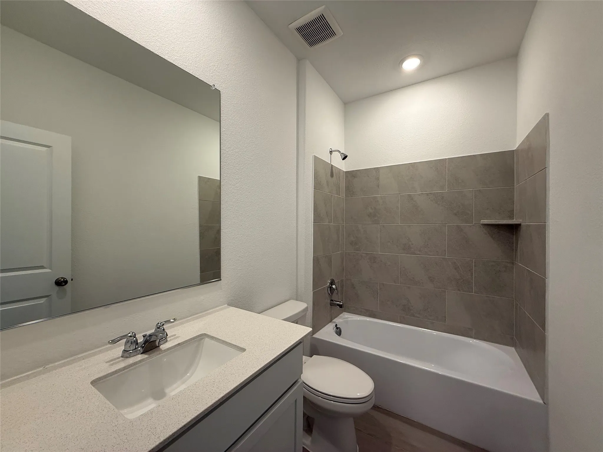Bathroom featuring a vanity with an integrated sink, polished chrome fixtures, a full-width mirror, and a tiled tub surround with an integrated shelf