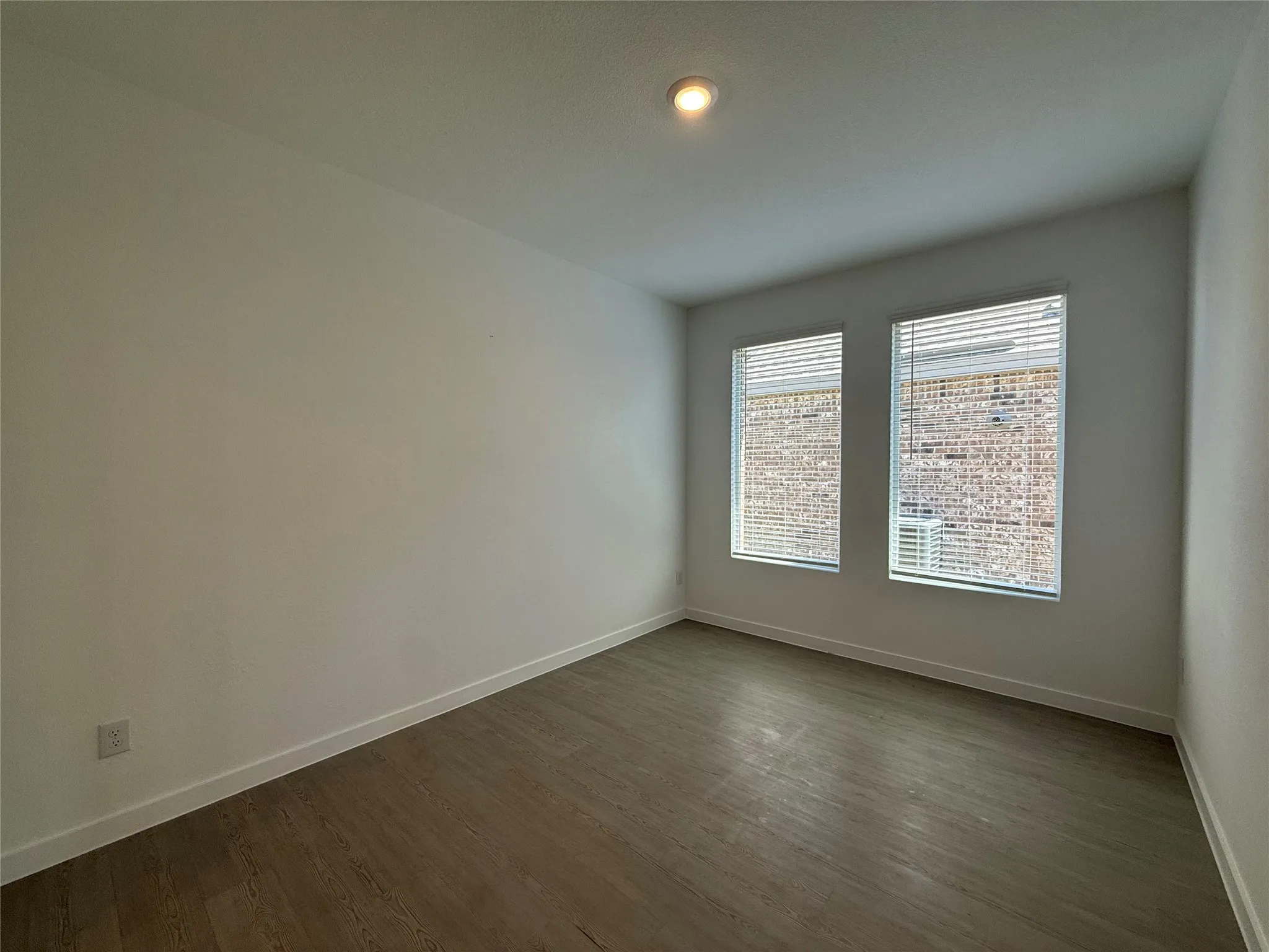 Recessed lighting, two large windows with blinds, light wood-finish flooring, and crisp white walls