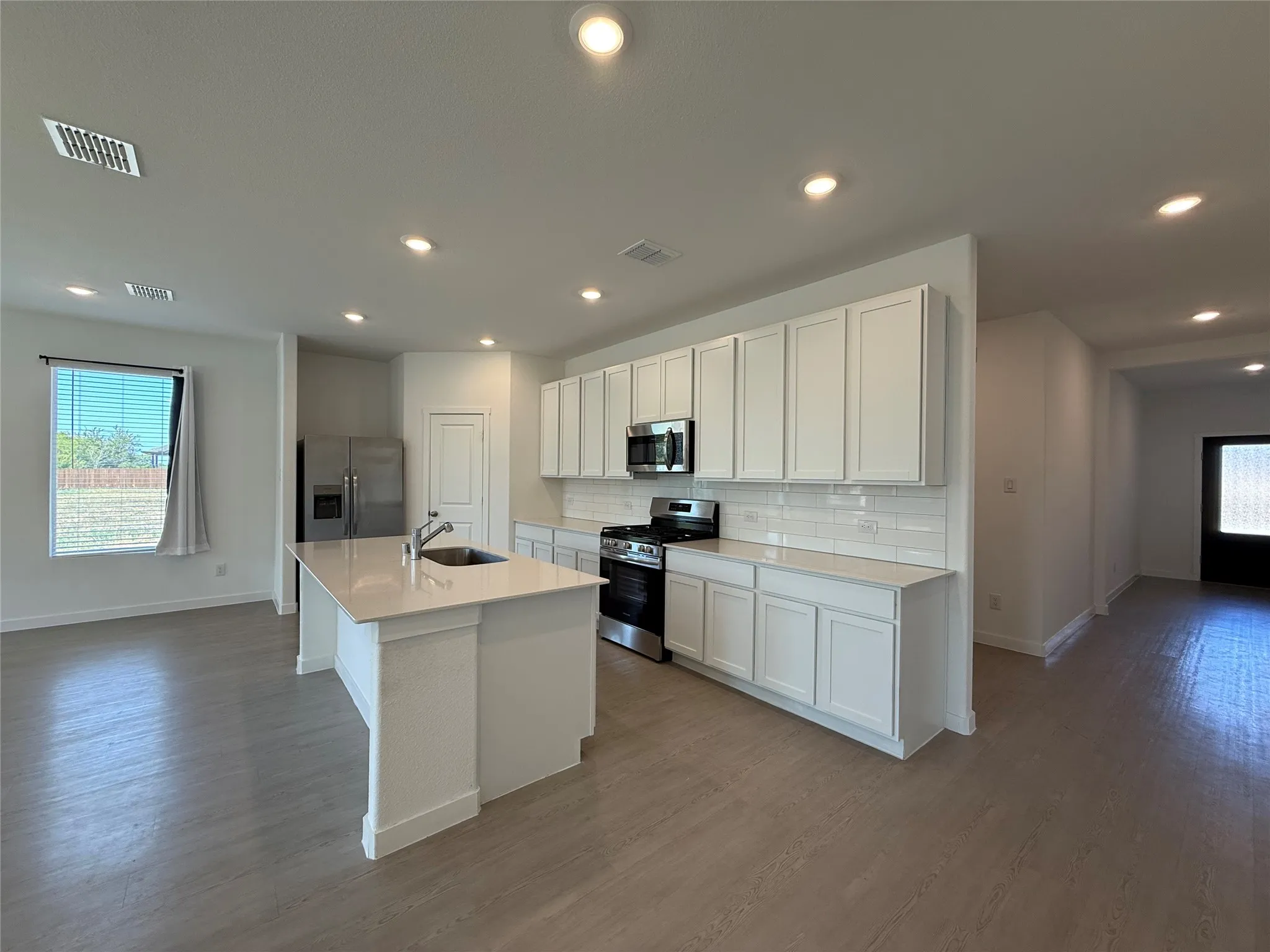 Kitchen featuring a central island with sink, stainless steel appliances, white cabinetry, and subway tile backsplash