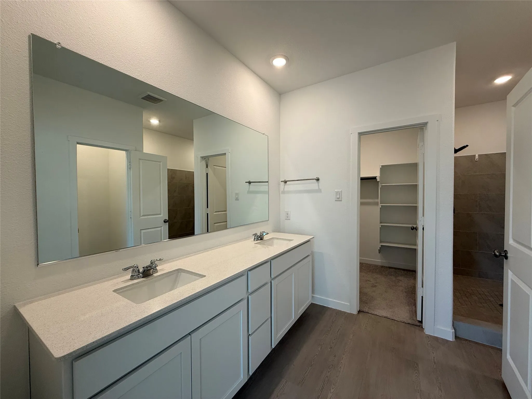 Dual vanity with light-toned countertop and integrated sinks, wood-finish flooring, and built-in shelving in an adjacent space