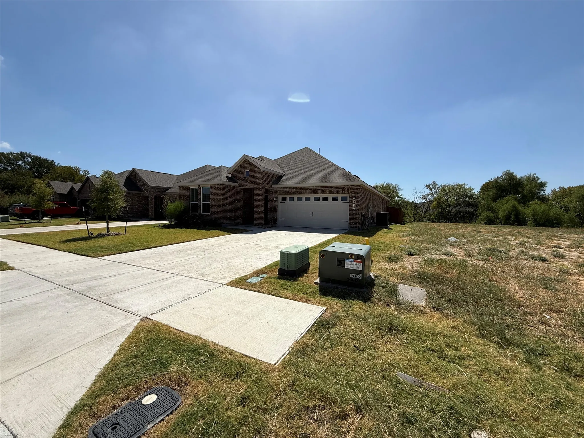 Brick exterior, attached garage, concrete driveway, front yard landscaping, natural terrain