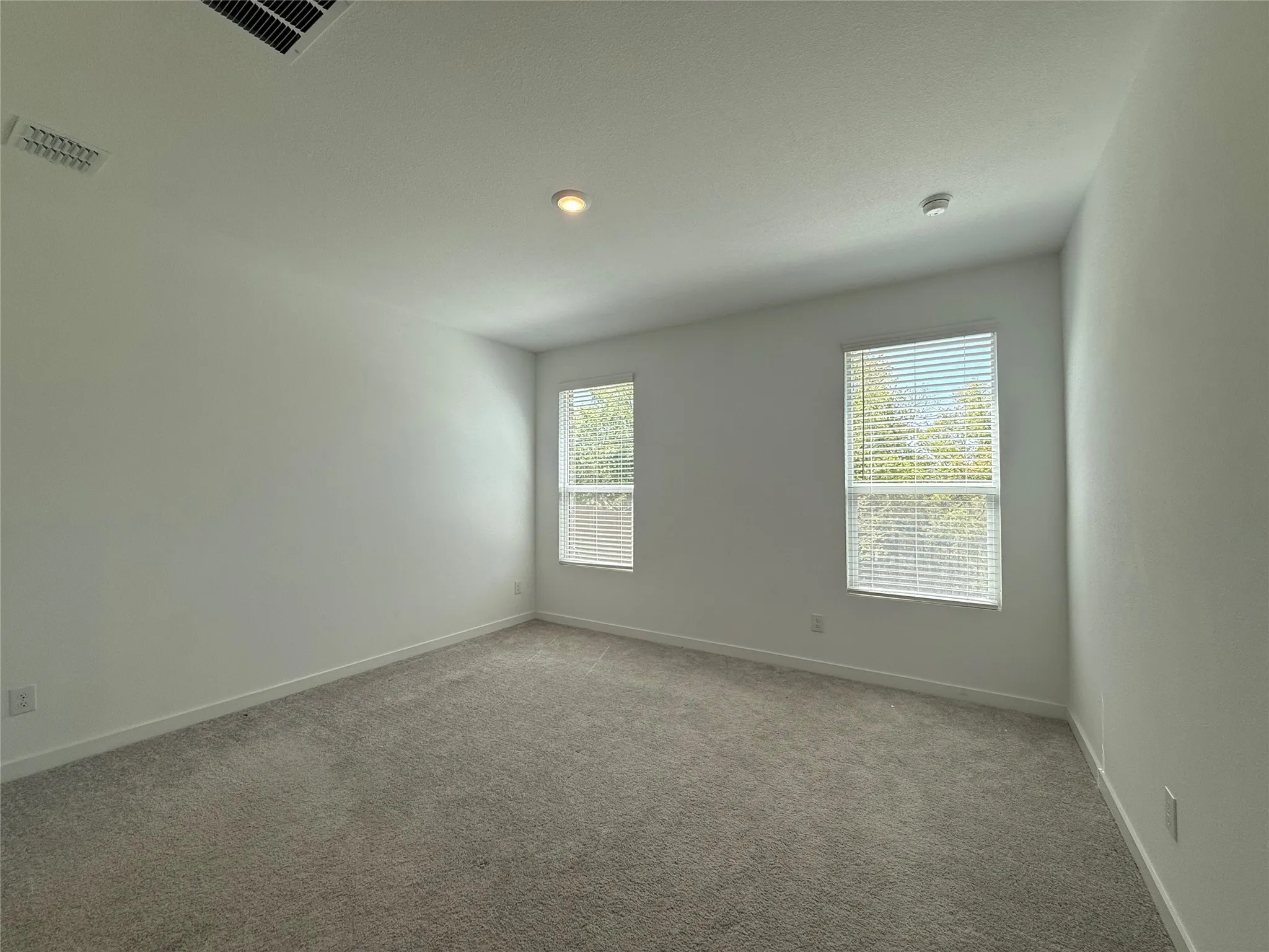 Light-toned wall-to-wall carpeting, two windows with blinds, recessed ceiling lighting, and crisp white walls